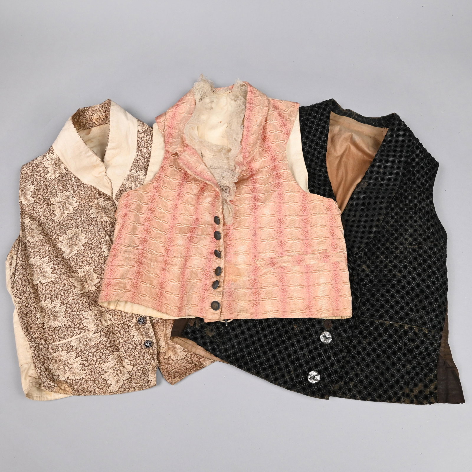 3 Gentlemen's Waistcoats (Vests), Mid-19th Century: The first printed in shades of brown and cream in an overall leaf pattern on a floral ground, glass opaque white and black striated buttons; the second in shades of pink and cream silk, embroidered in