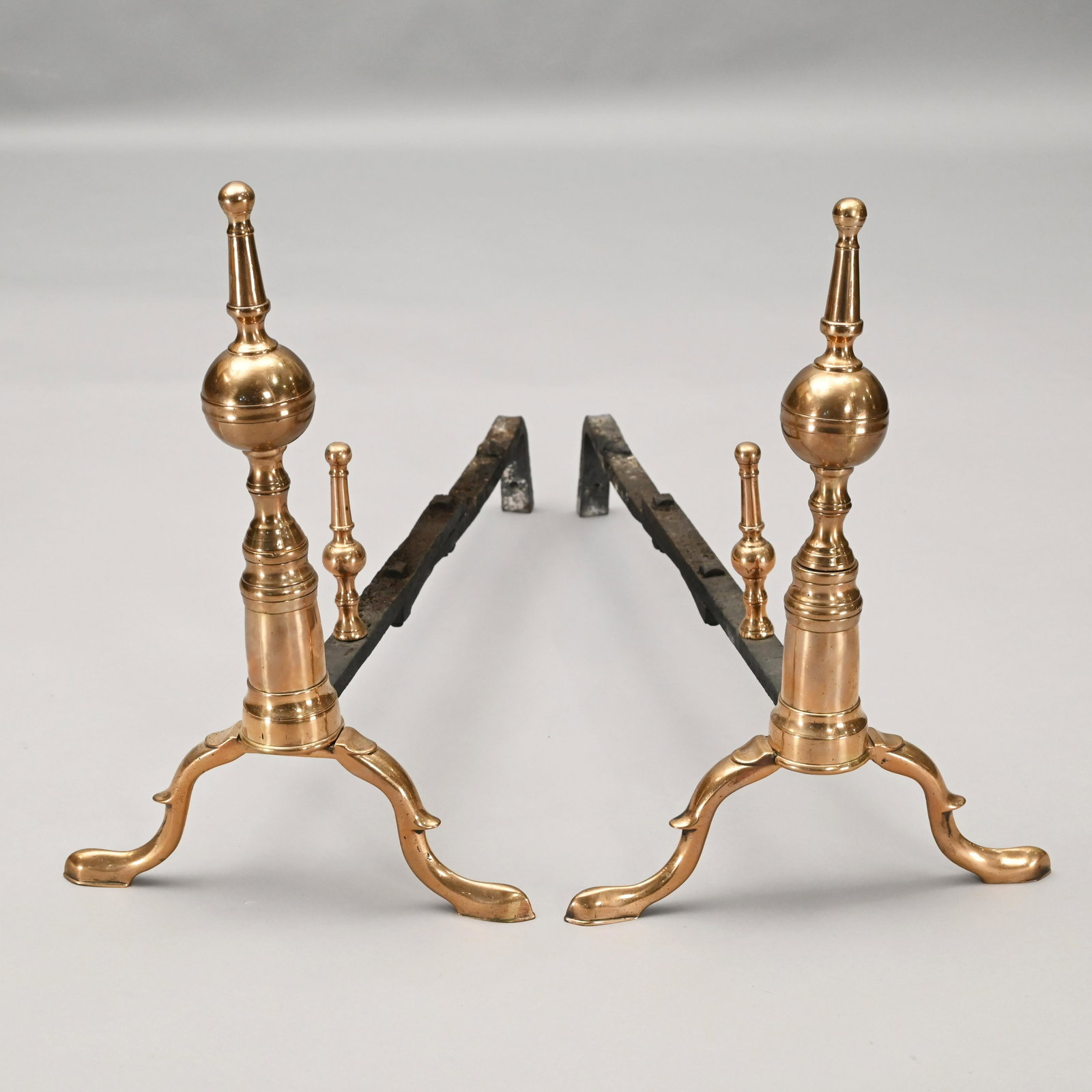 Pair of Federal Bell Metal Steeple-Top Andirons: Each turned standard surmounted by a belted ball and steeple finial, raised on spurred cabriole legs ending in pad feet, the log stops of a conforming form, the dogs extended. H: 17 in., W: 11.5 in., 