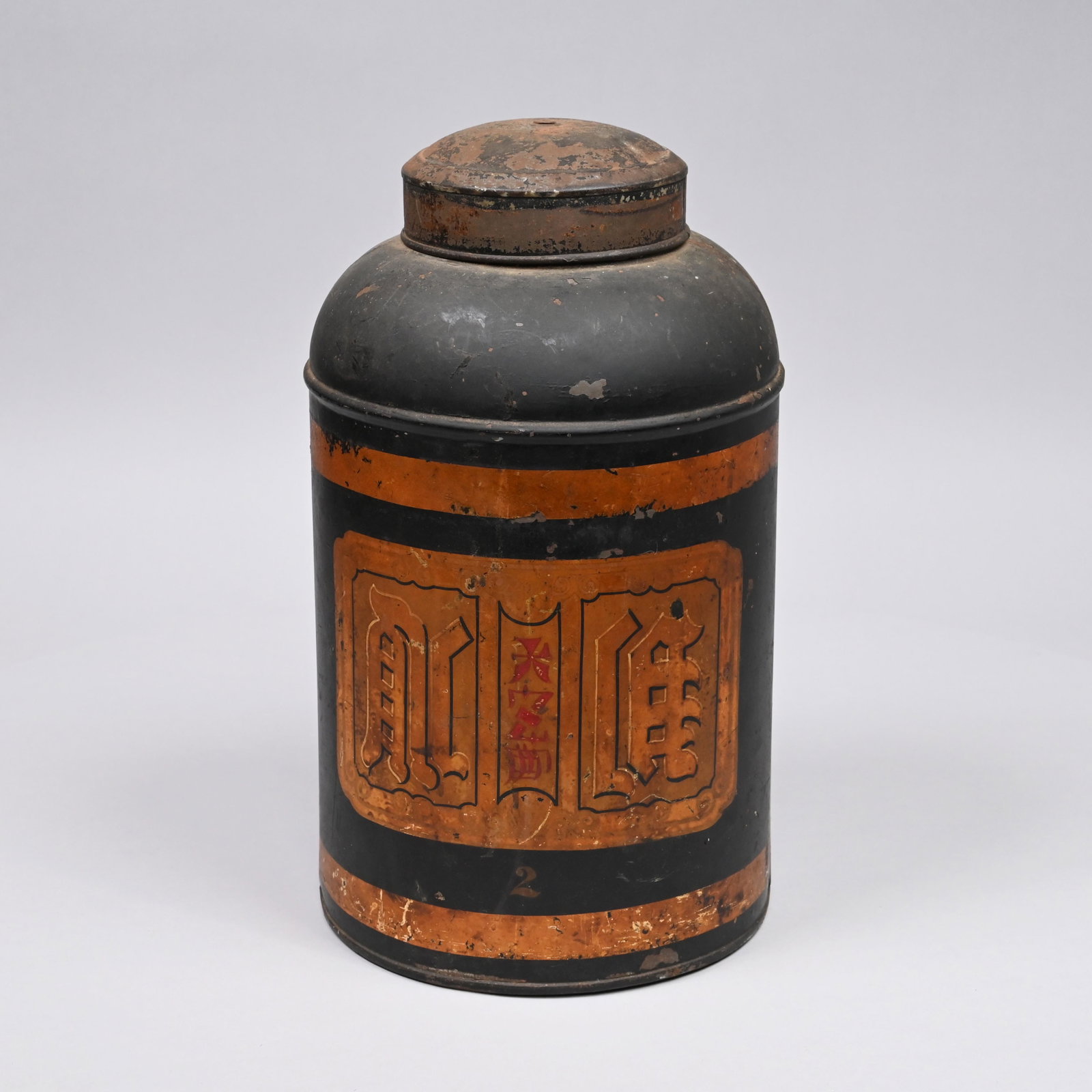 English Tin Chinoiserie Tea Canister, 19th Century: Painted and stencilled in gold and red with a panel of Chinese characters, the canister and domed cover surrounded by gold banding, all reserved on a black ground. H: 15.5 in., W: 9 in., D: 9 in.