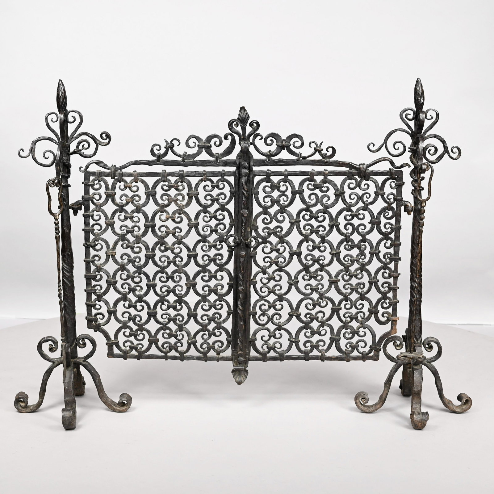 Arts & Crafts Wrought-Iron Fireplace Screen &Tools: Arts & Crafts Wrought-Iron Fireplace Screen and Pair of Tools, Early Twentieth Century. The screen cast of opposing interlocked C-scrolls, mounted on spiral-wrythen posts surmounted by flame finials w