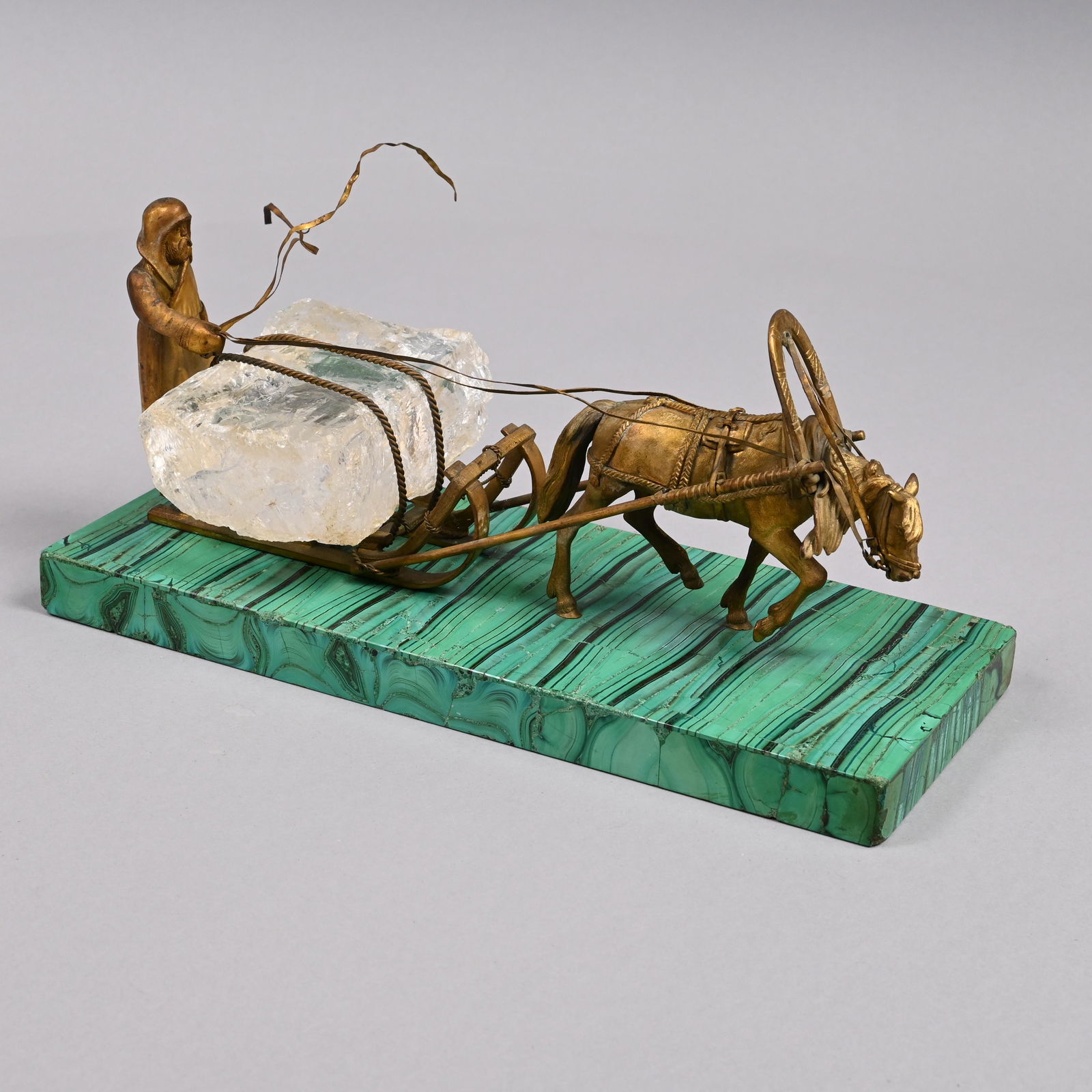 Russian Malachite, Gilt-Metal & Rock Crystal Group: Modelled as an ice harvester with a large rock crystal block of ice on his sled, and driving a horse in traditional harness, mounted on a malachite base. H: 4.75 in., W: 10.625 in., D: 4.375 in.