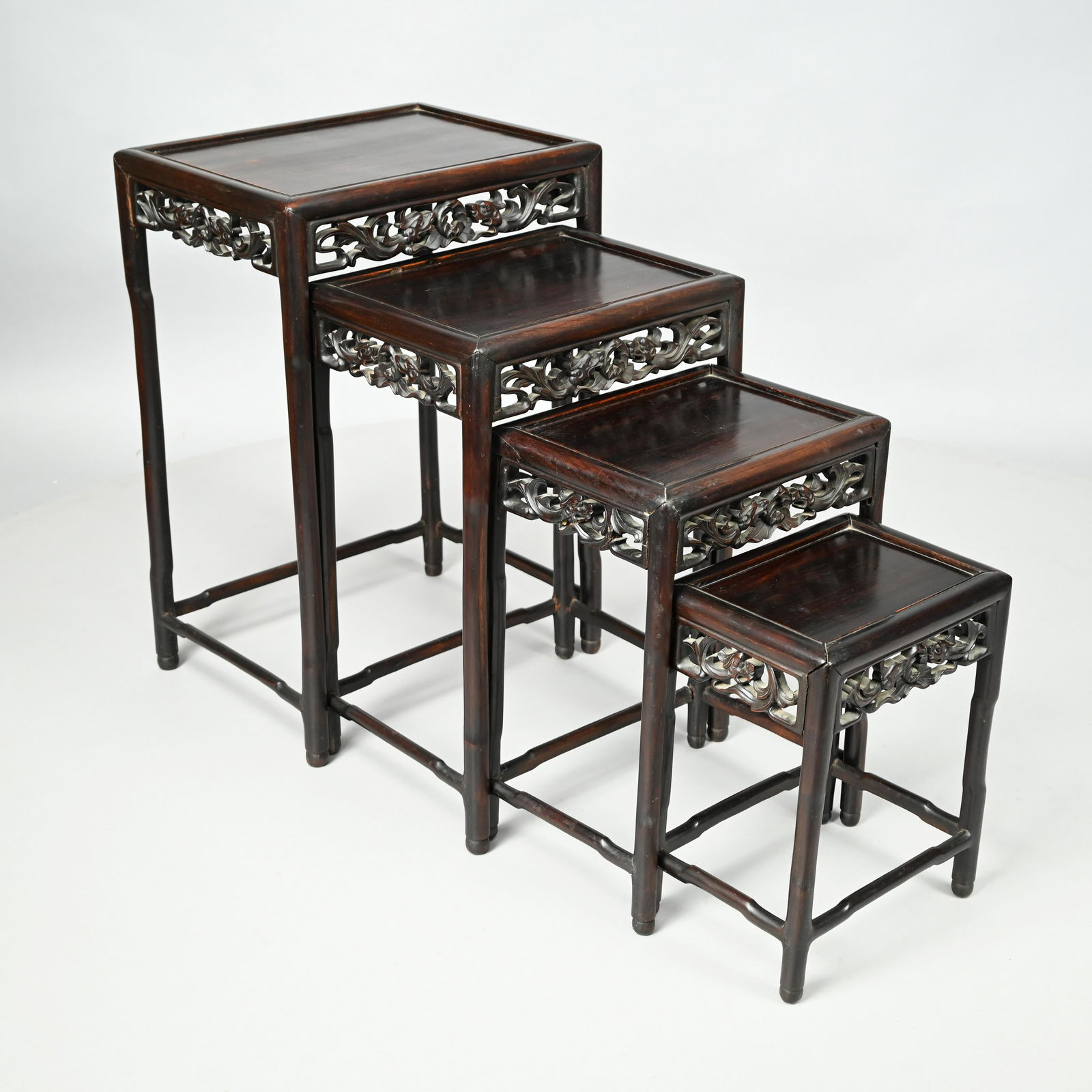 Set of Four Chinese Carved Hardwood Nesting Tables: Early Twentieth Century. Each inset rectangular top above the frieze pierce-carved on each side with a pair of dragons centering a stylized fiery pearl, raised on faux bamboo legs joined by a shaped b