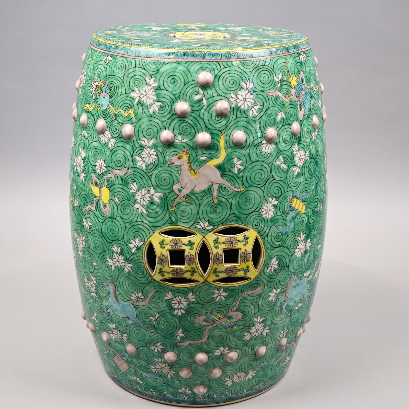 Chinese Export Porcelain Famille Rose Garden Seat: Painted with yellow, blue, rose and white leaping horses and beribboned leaves, fruit and vessels on a white floral and green scroll ground, pierced on the top with a yellow cash symbol and the sides 