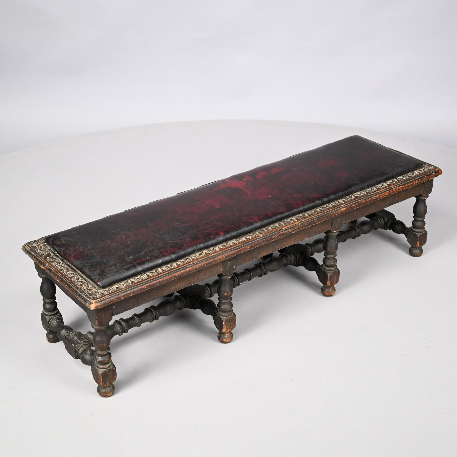 Jacobean Revival Carved Oak Fireside Bench: Circa 1900. The upholstered padded top within a border of carved leaves, raised on block-and-ring turned legs joined by H-form stretchers. H: 11.75 in., W: 13 in., D: 41.25 in.