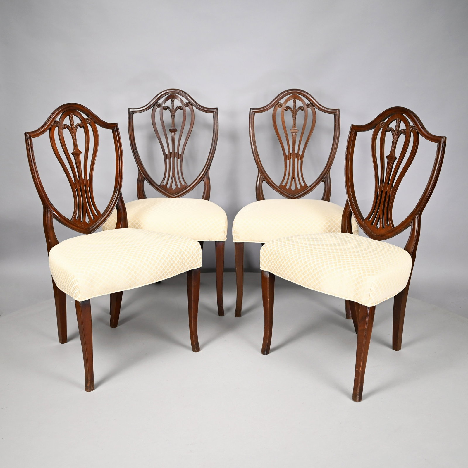 Set of Four Federal Mahogany Dining Chairs: Each molded shield-shaped back enclosing a pierce-carved splat centering a Prince-of-Wales plume within flowerheads, the over-upholstered seat raised on slightly curved molded square tapered legs. H: 