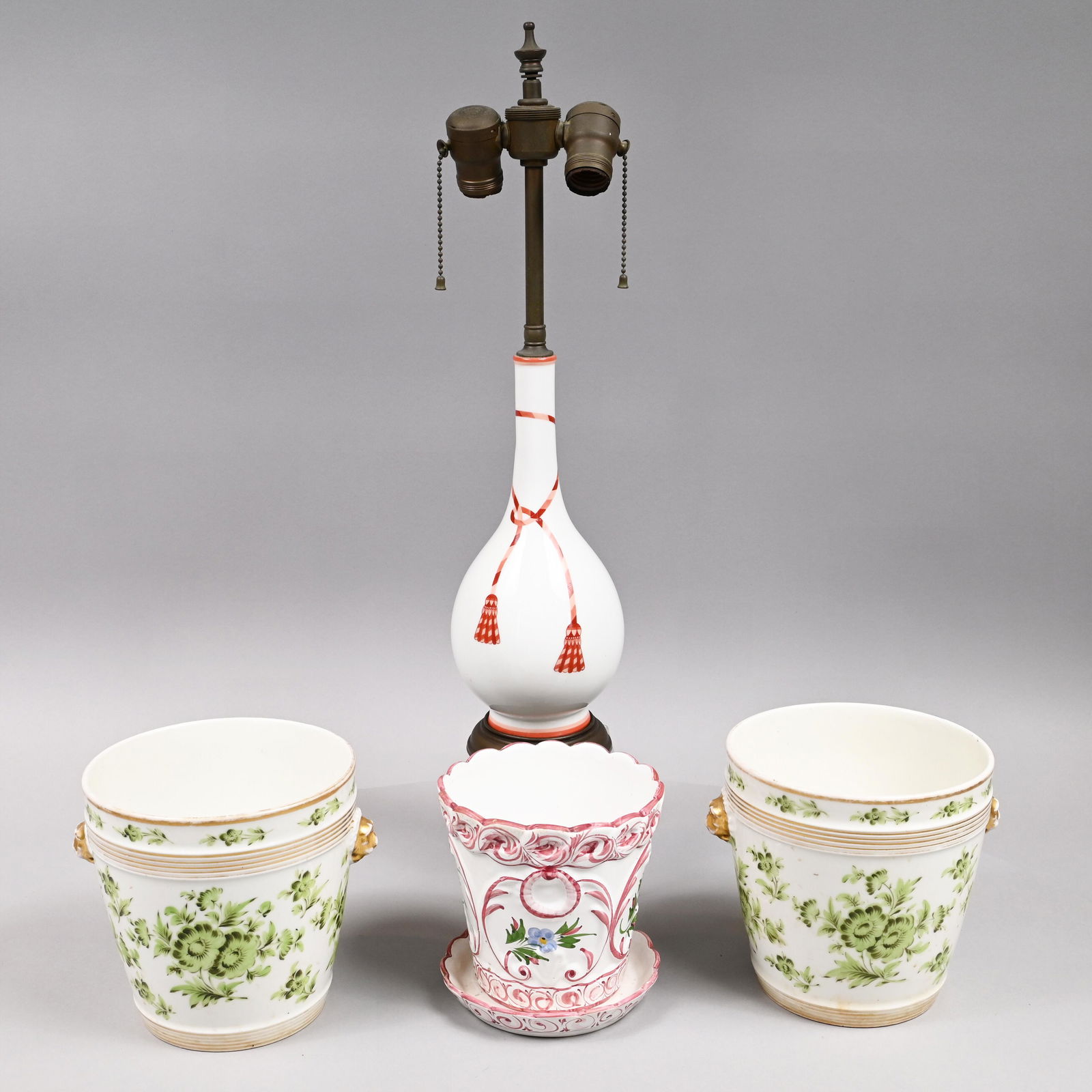 Four Continental Porcelain Decorative Objects: Twentieth Century. Comprising a pair of Paris porcelain jardinieres, each painted in green with floral sprays, gilt lion mask handles; a Portuguese flower pot and stand, molded with pink cartouches en
