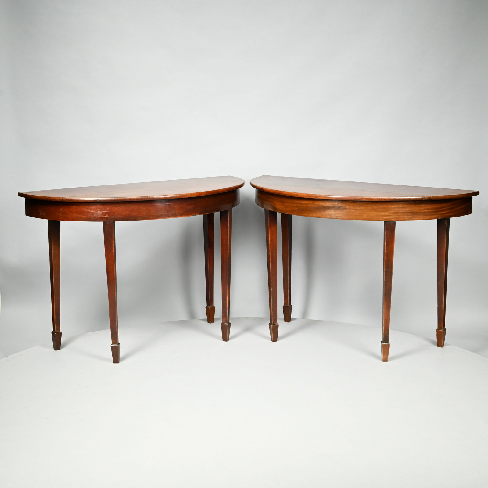 Pair of George III Style Mahogany Console Tables: Each demilune top above a plain frieze, raised on square tapered legs ending in spade feet. H: 30 in., W: 45.5 in., D: 20 in.