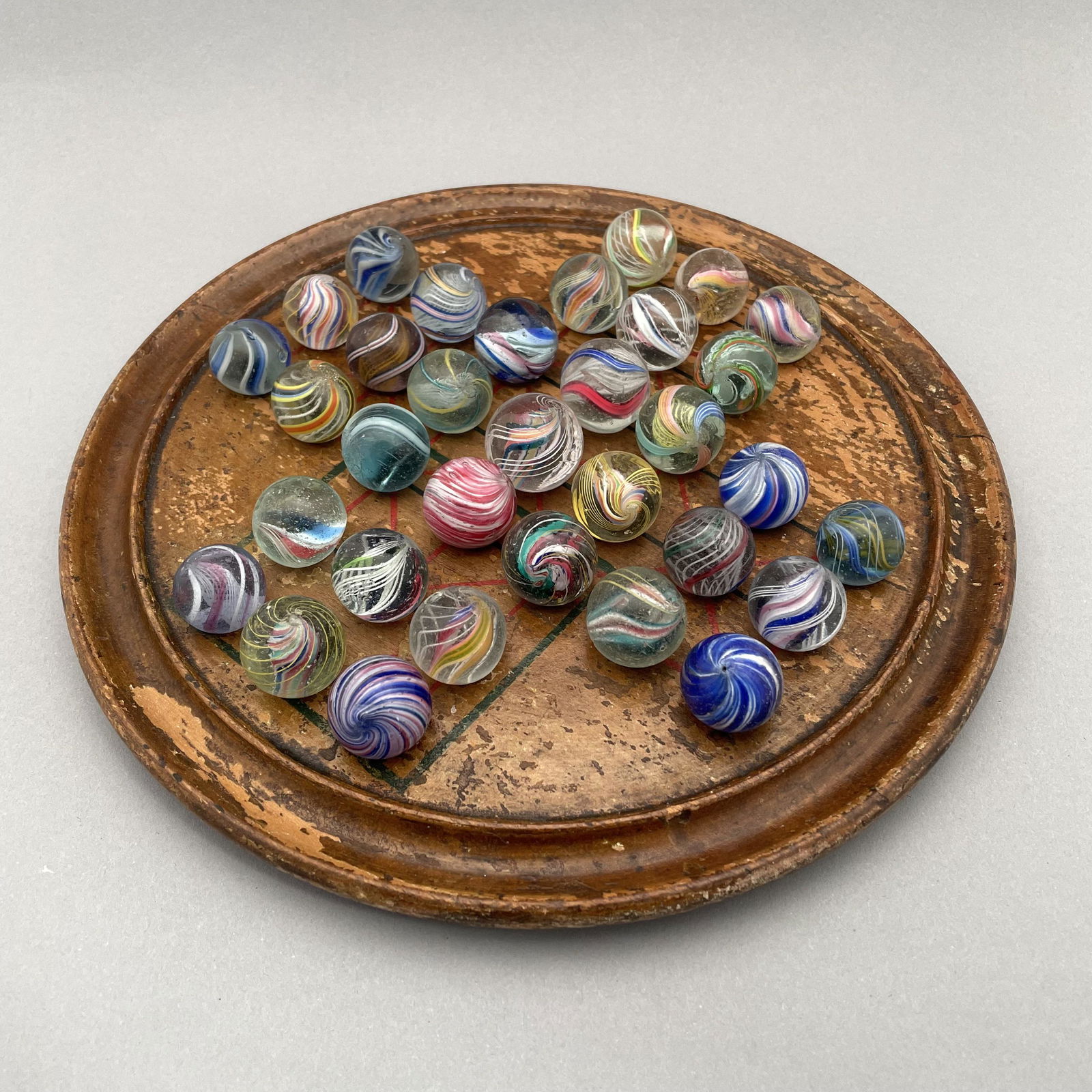 General Grant Marble Board, Thirty-Three Marbles: The marbles handmade and comprising swirls and onion skins. Approximate range of diameters: 91/128 to 111/128 inches Board: Diam: 8.375 in., D: .5 in.