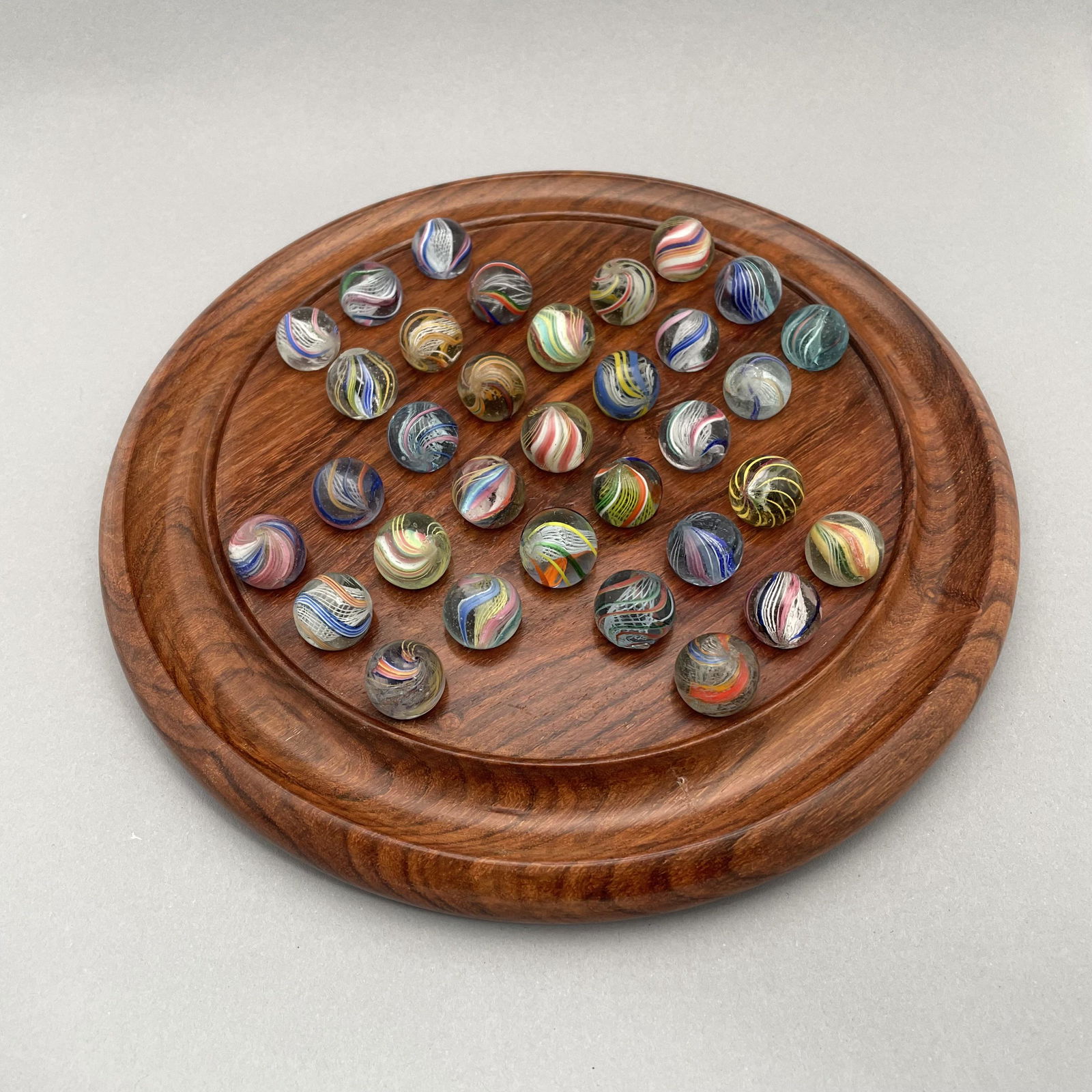 General Grant Marble Board, Thirty-Three Marbles: The marbles handmade and comprising swirls. Approximate range of diameters: 21/32 to 89/128 inch. Board: Diam: 9 in., D: 1 in.