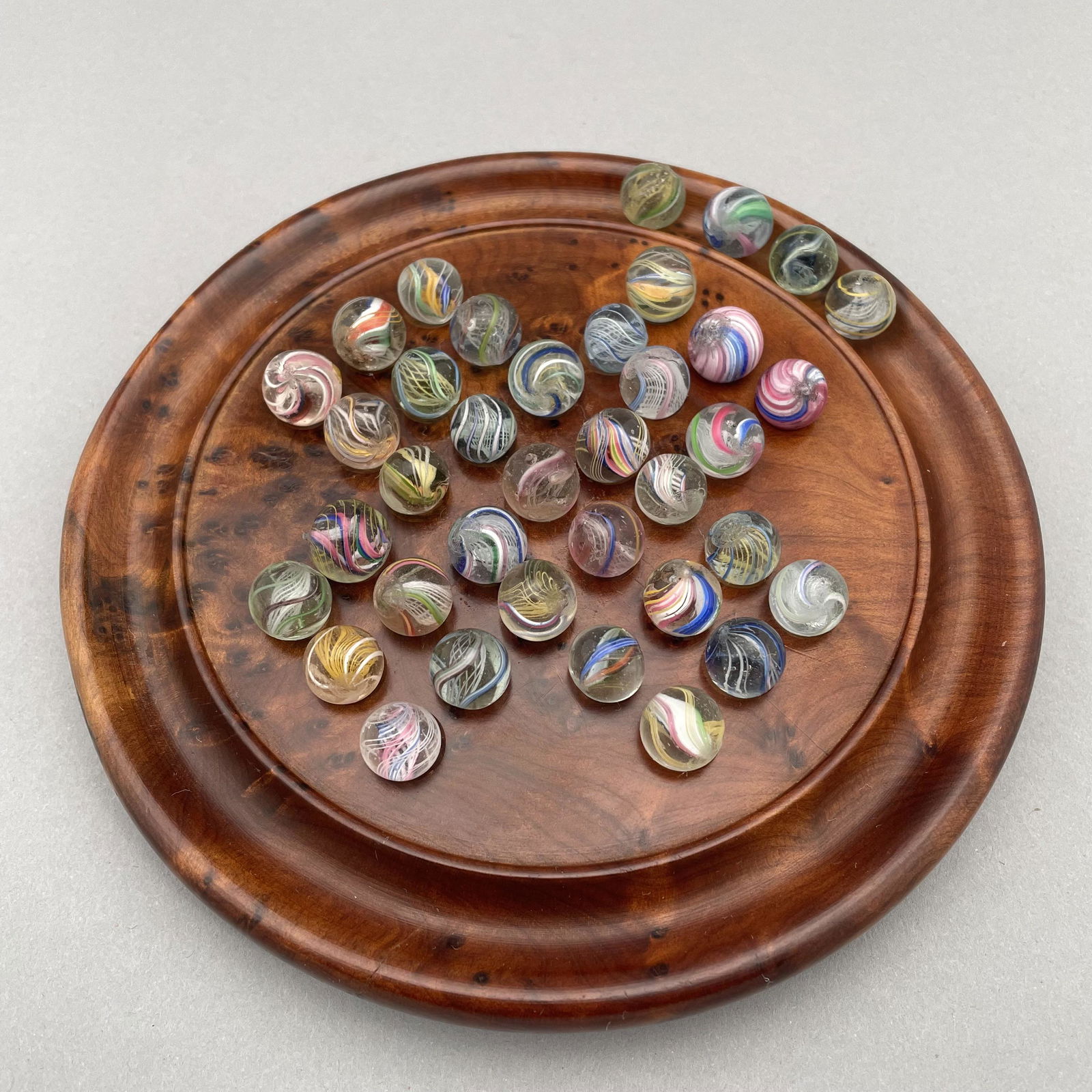 Solitaire Board, Thirty-Seven Pee Wee Marbles: The marbles handmade and comprising swirls and onion skins. Approximate range of diameters: 27/64 to 63/128 inch Board: Diam: 6.125 in., D: .625 in.