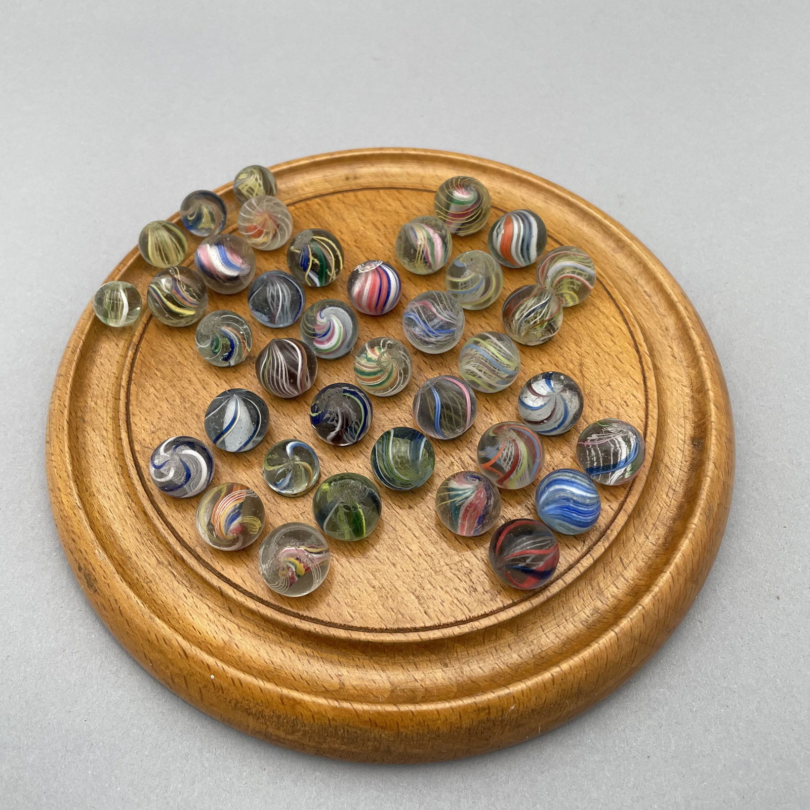 Solitaire Marble Board, Thirty-Seven Marbles: The marbles handmade and comprising swirls. Approximate range of diameters: 57/128 to 73/128 inches Board: Diam: 6.5 in., D: .75 in.