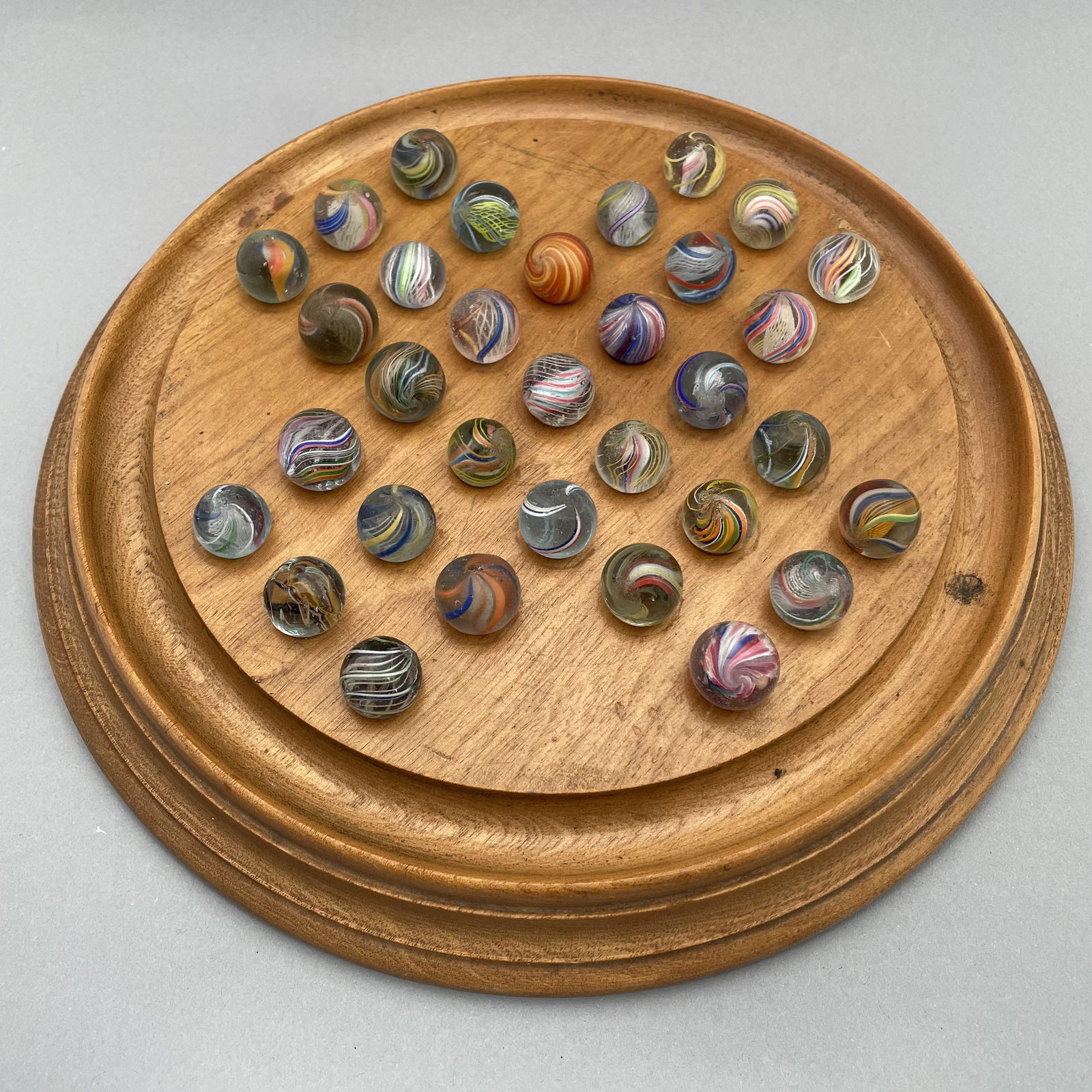 Solitaire Board, Thirty-Three Pee Wee Marbles: The marbles handmade and comprising swirls and onion skins. Approximate range of diam: 79/128 to 93/128 inch Board: Diam: 9.75 in., D: 1.25 in.
