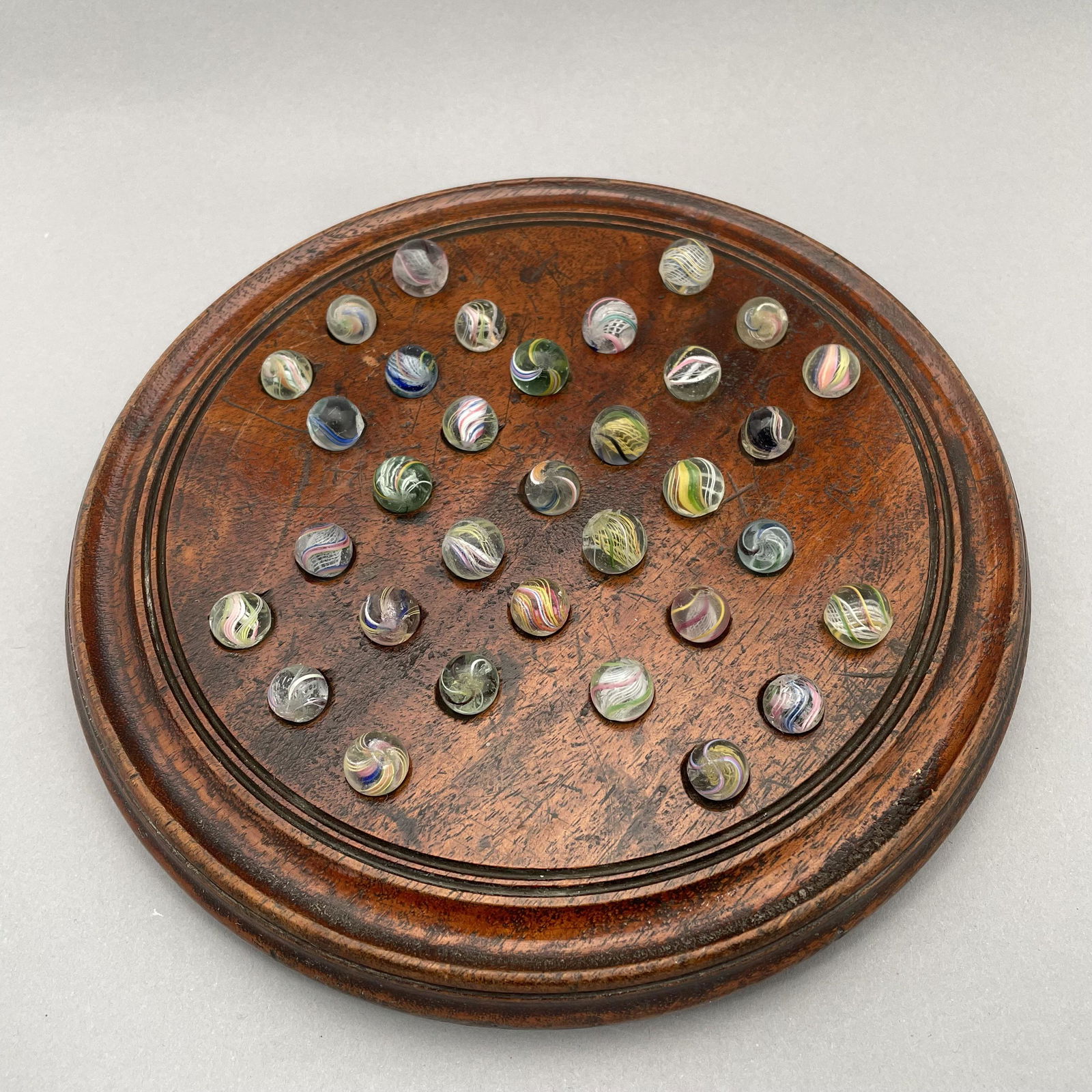Solitaire Board, Thirty-Three Pee Wee Marbles: The marbles handmade and comprising swirls. Approximate range of diam: 61/128 to 75/128 inch Board: Diam: 9 in., D: 1 in.