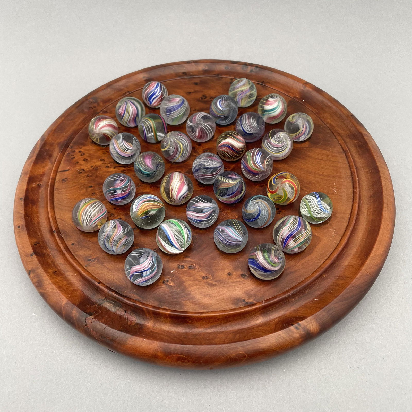 Solitaire Board with Thirty-Three Marbles: The marbles handmade and comprising swirls. Approximate range of diam: 81/128 to 3/4 in. Board: Diam. 8.25 in., D: .875 in.