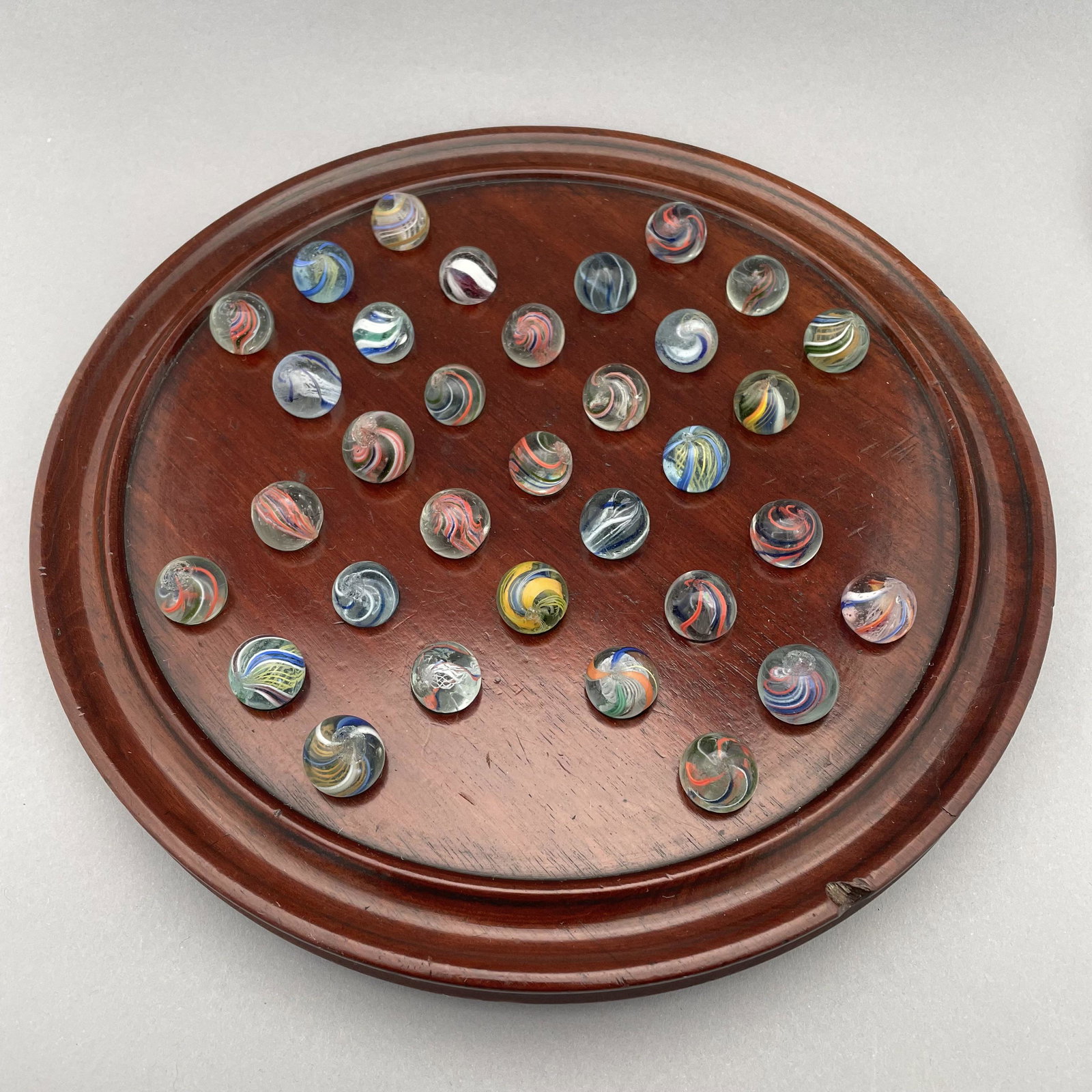 Solitaire Board with Thirty-Three Marbles: The marbles handmade and comprising swirls. Approximate range of diam: 79/128 to 23/32 in. Board: Diam: 10 in., D: 1 in.
