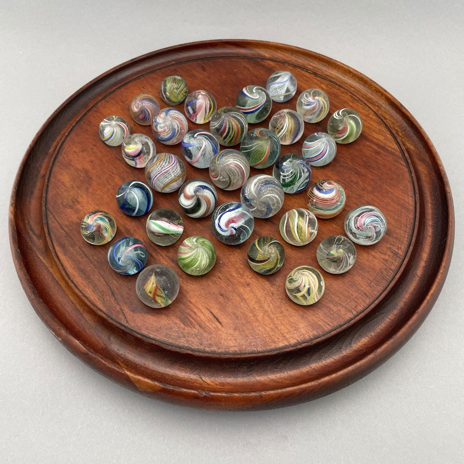 Solitaire Board with Thirty-Three Marbles: The marbles handmade and comprising swirls. Approximate range of diam: 87/128 to 117/128 in. Board: Diam: 10 in., D: 1.125 in.