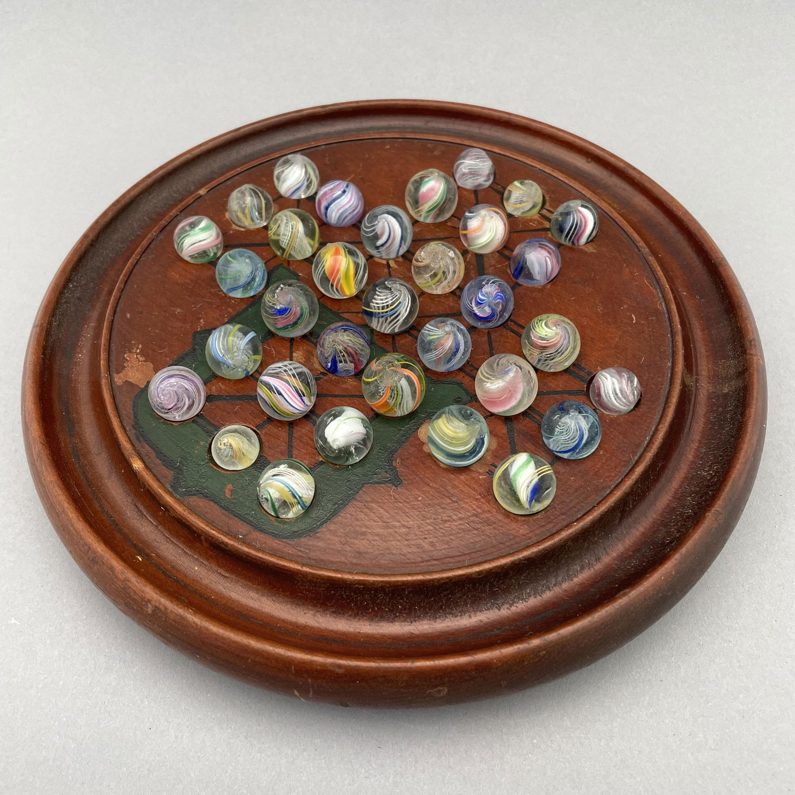 Solitaire Board with Thirty-Three Pee Wee Marbles: The marbles handmade and comprising swirls. Approximate range of diam: 13/32 to 81/128 in. Board: Diam: 7.625 in., D: 1.125 in.