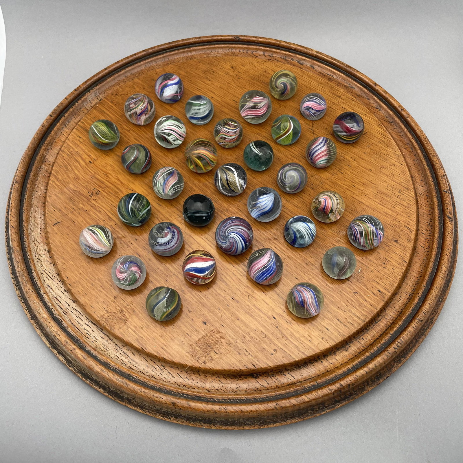 Solitaire Board with Thirty-Three Marbles: The marbles handmade and comprising swirls. Approximate range of diam: 93/128 to 57/64 in. Board: Diam: 11.625 in., D: 1 in.