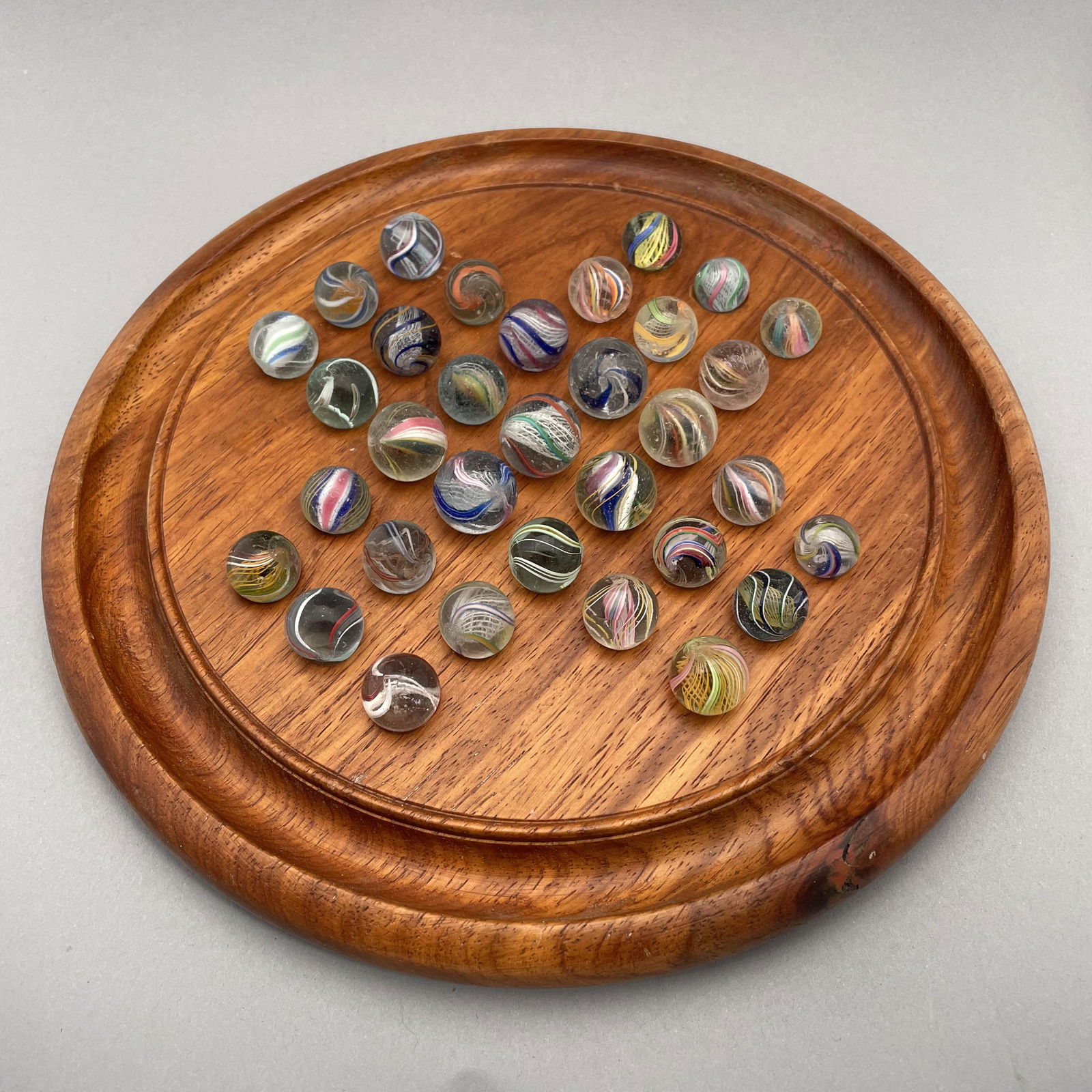 Solitaire Board with Thirty-Three Marbles: The marbles handmade and comprising swirls. Approximate range of diam: 9/16 to 101/128 in. Board: Diam: 9.75 in., D: .75 in.