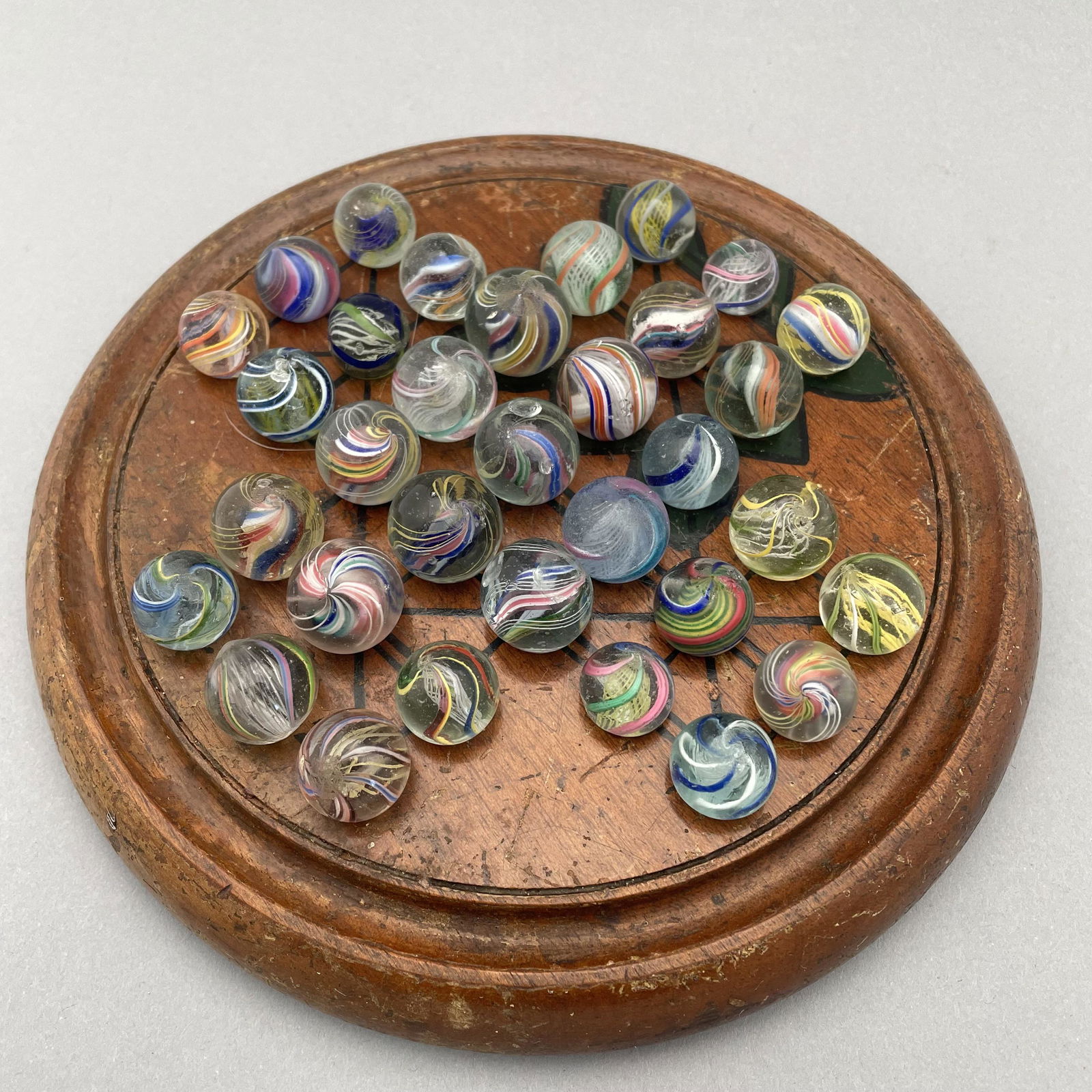 Solitaire Board with Thirty-Three Marbles: The marbles handmade and comprising swirls. Approximate range of diam: 75/128 to 101/128 in. Board: Diam: 7.625 in., D: 1 in.