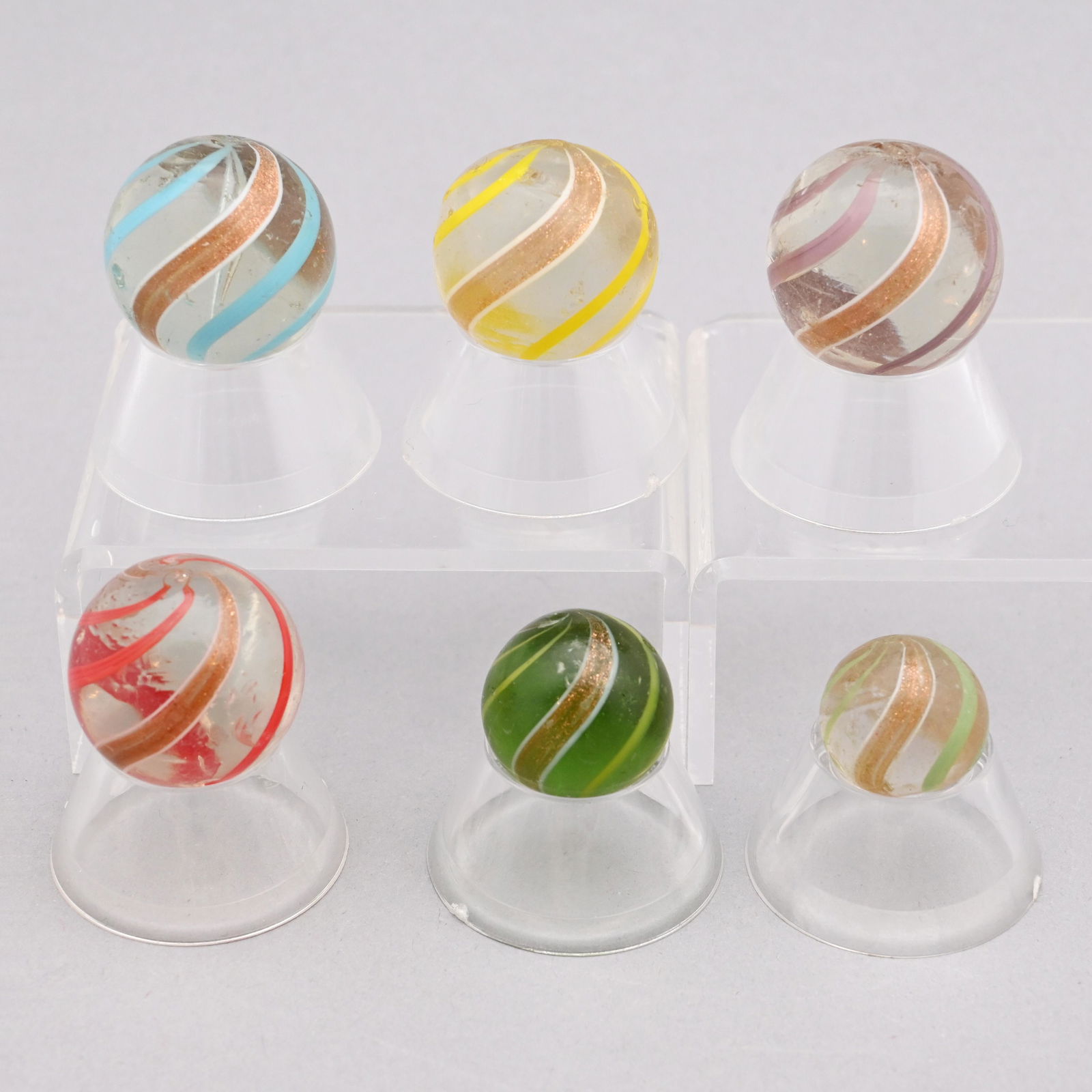 Six Banded Gold Lutz Marbles: In gold and shades of sky blue, dark green, red, rose, yellow and white swirls. Approximate range of diam: 91/128 inch to 1 1/64 in.
