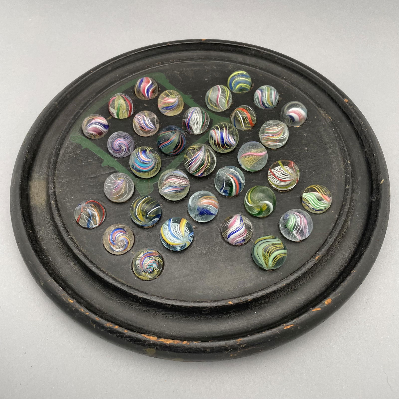Solitaire Board with Thirty-Three Marbles: The marbles handmade and comprising swirls. Approximate range of diam: 87/128 to 109/128 in. Board: Diam: 9.75 in., D: 1 in.