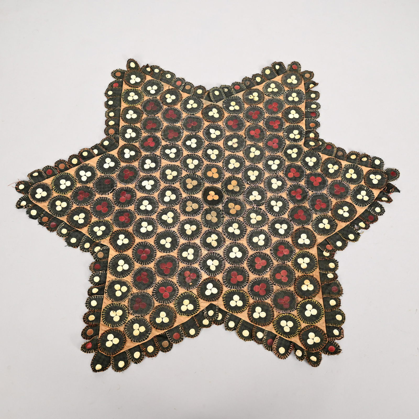 Embroidered and Appliqued Felt Penny Table Throw: Early Twentieth Century. Star-shaped, worked in rows of alternating groups of white, maroon and grey dots on a black fabric circle, all stitched in various colors onto a light brown linen field within