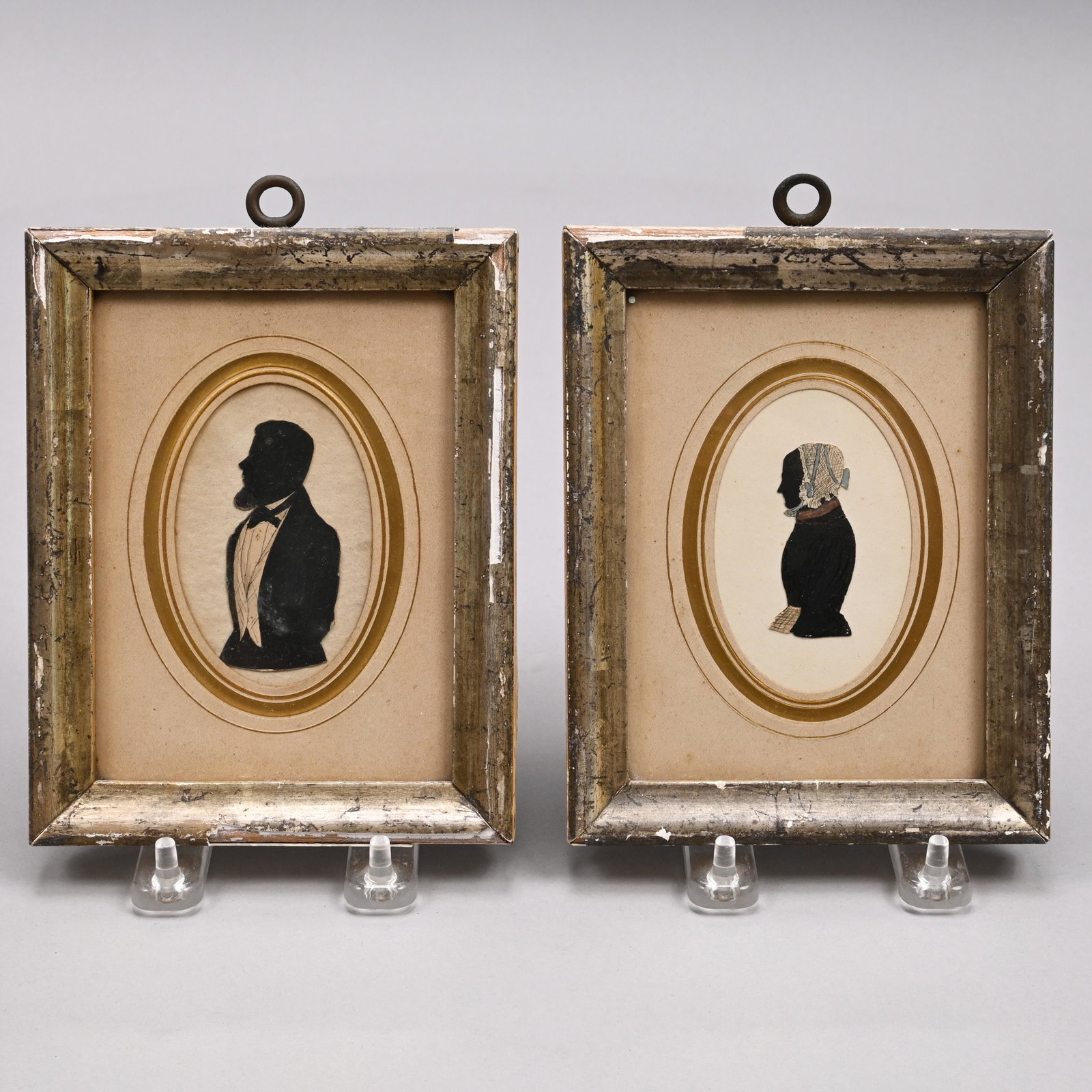 Pair of German Silhouette Portraits, 19th Century: Cut-out silhouettes, watercolor and ink on paper, the first depicting a lady attired in a white lace cap with blue ribbon, and a black dress with white apron, inscribed on the reverse "Anna Margaretha