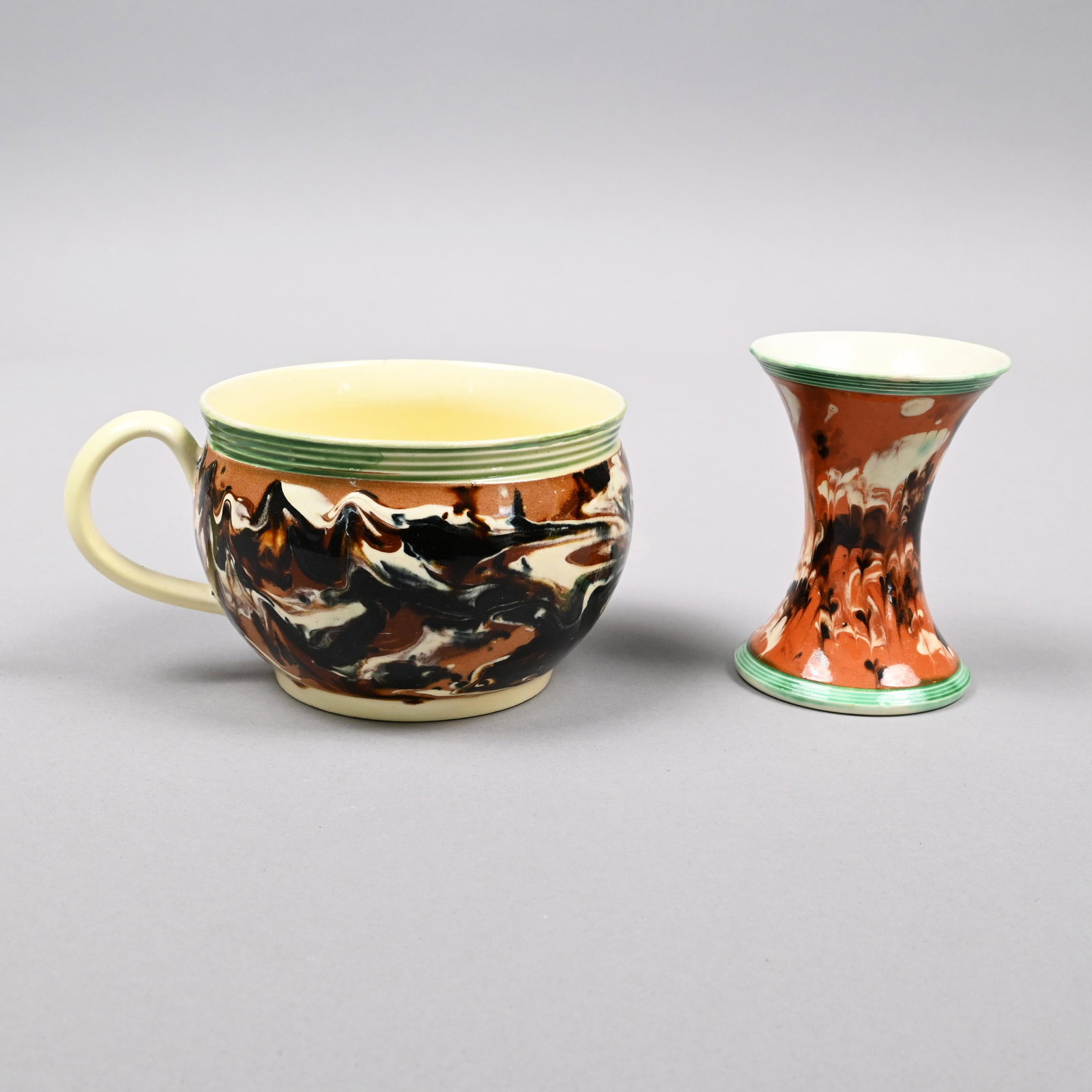 British Creamware Mochaware Porringer & Spill Vase: 1790-1810. The porringer slip-marbled in black, brown, dark blue and white on a pale brown field, beneath a rouletted green-glazed reeded border; the spill vase slip-marbled and combed in dark brown a