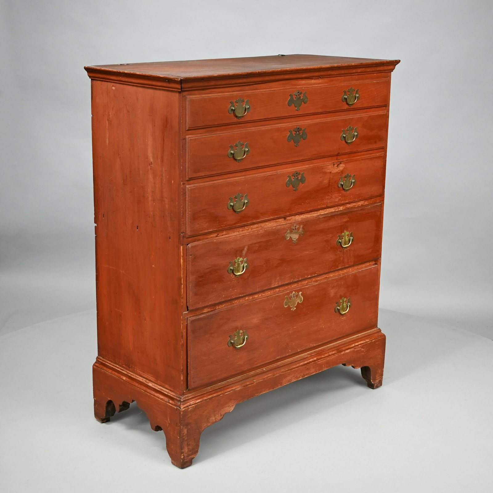 New England Chippendale Pine Blanket Chest: Early Nineteenth Century. In red paint, the rectangular top lifting to a compartment simulating three molded drawers on the front, above two graduated working drawers, raised on a bracket base. H: 46 