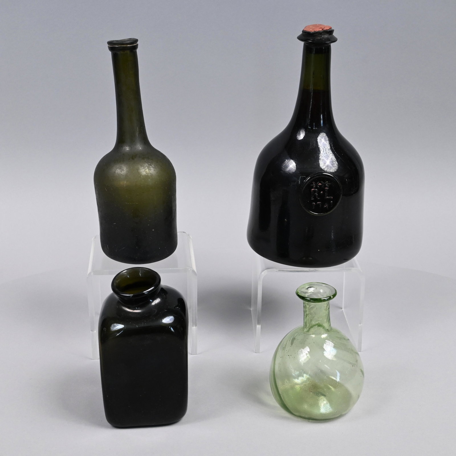 Three English Blown-Molded Glass Bottles & Another: Eighteenth-Early Nineteenth Century. Comprising a wine bottle, the seal embossed "**/ R*L/ 1743," a mallet bottle and a small case bottle, all in dark green glass; and a pattern-molded spirally writhe
