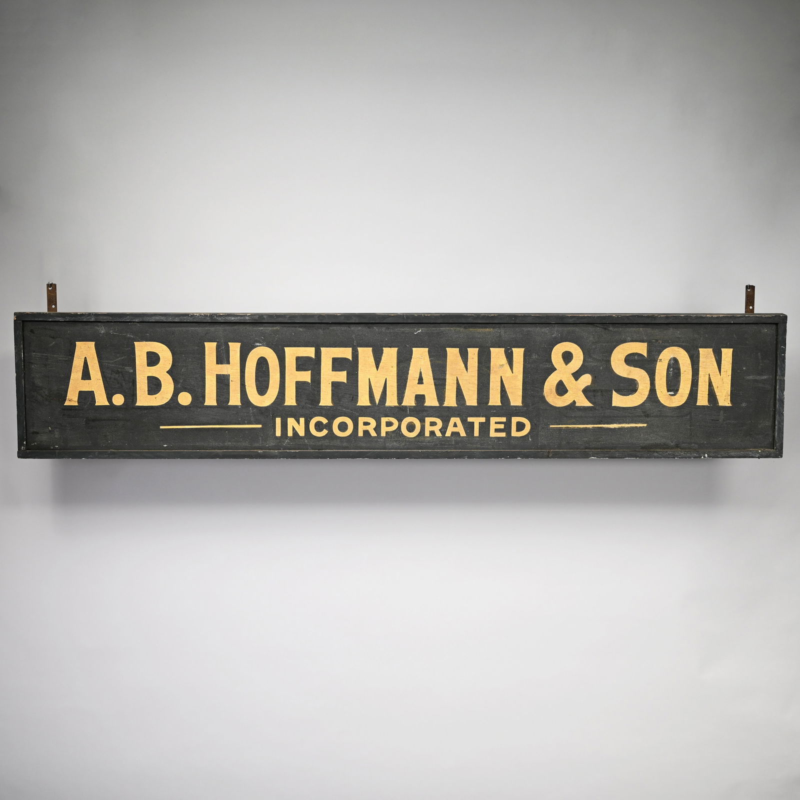 "A.B. HOFFMAN & SON" Painted Wood Trade Sign: Painted "A.B. HOFFMAN & SON, INCORPORATED" in gold letters on a black ground and within applied edges. H: 15.25 In., W: 80.75 in., D: 2 in.