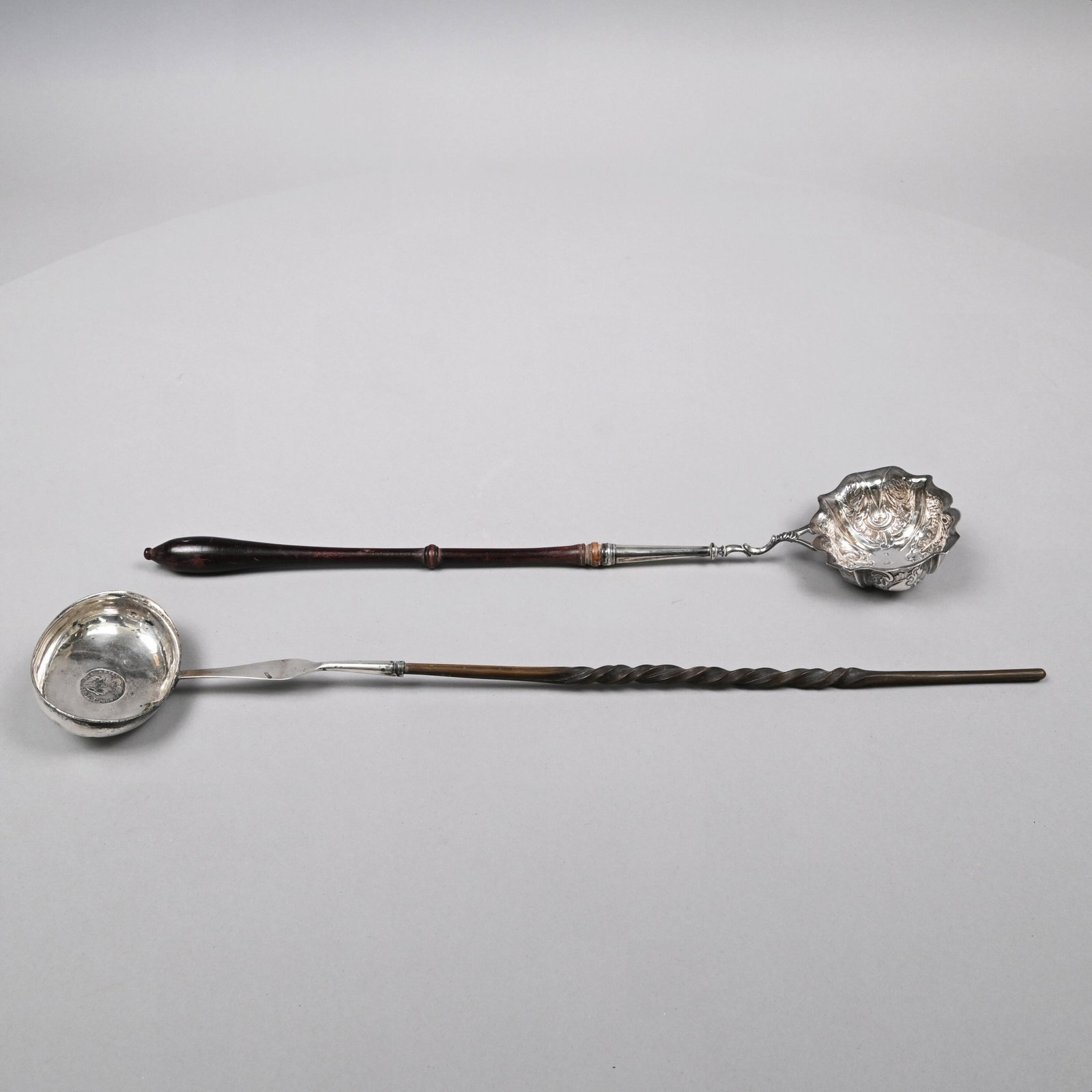 Two George II Silver Toddy Ladles, Eighteenth Cent: The first Fuller White, London, 1746-58, the bowl repousse with shells, foliage and ruffled cartouches, maker's mark "FW" to center of bowl and town mark, affixed with an ebonized wood turned handle; 