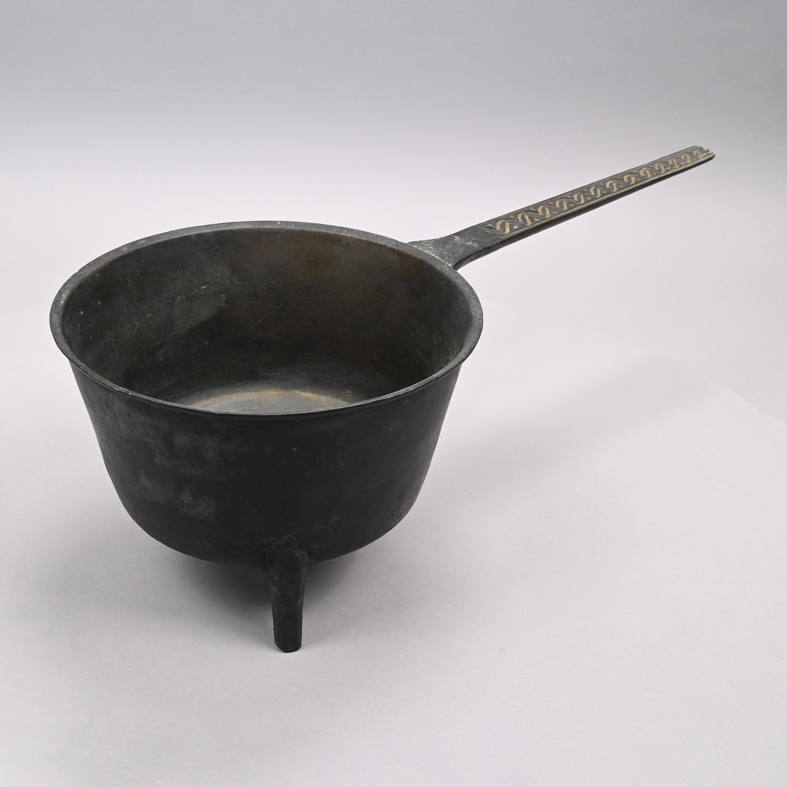 English Cast Bronze Posnet Pot, Eighteenth Century: The handle cast with a dot and wrigglework band, on three feet. Provenance: Sotheby's, New York, lot 1357. H: 7.5 in., W: 22.5 in., D: 10 in.