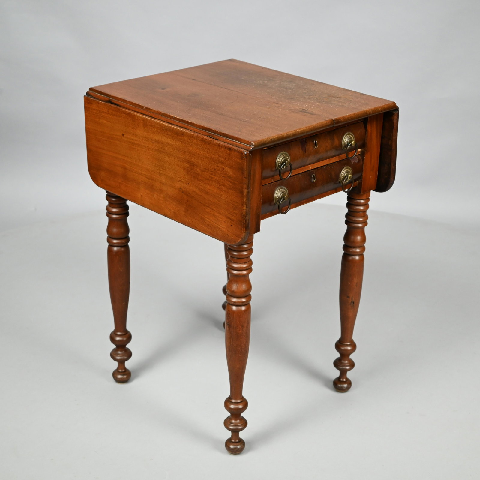 Sheraton Mahogany Drop-Leaf Work Table, Circa 1820: The rectangular top with drop-leaves above two convex-fronted drawers, raised on spool-turned legs ending in cuffs and ball feet. H: 29 in., W: (Closed) 18.5. in., (Open) 33.5 in., D: 20 in.