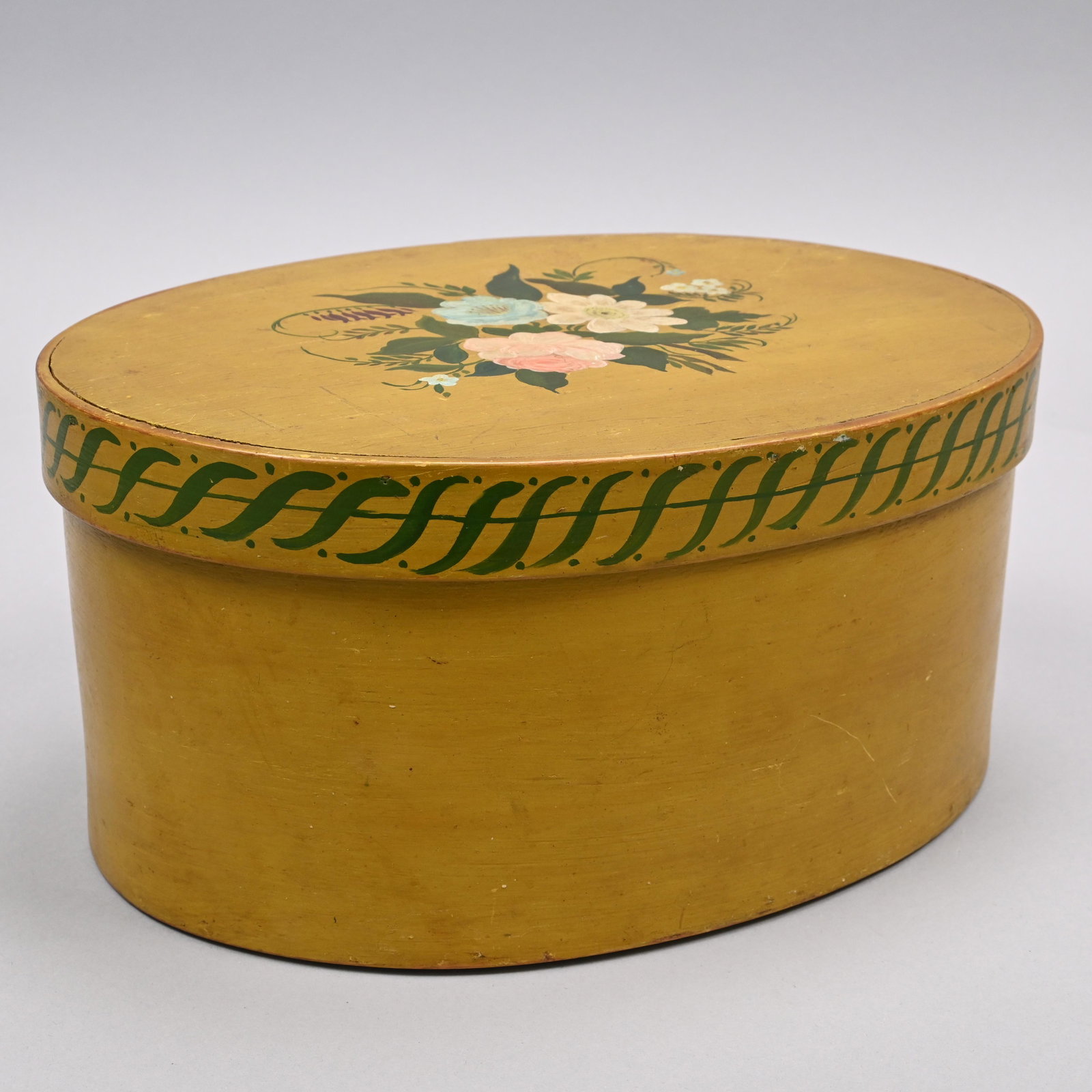 Shaker Painted Pine Oval Pantry Box, Signed: In mustard paint, the box of four finger construction, the lid painted with a floral arrangement and the edges surrounded by a border of "S" flourishes, painted conjoined initials "IHJ" beneath. H: 6 
