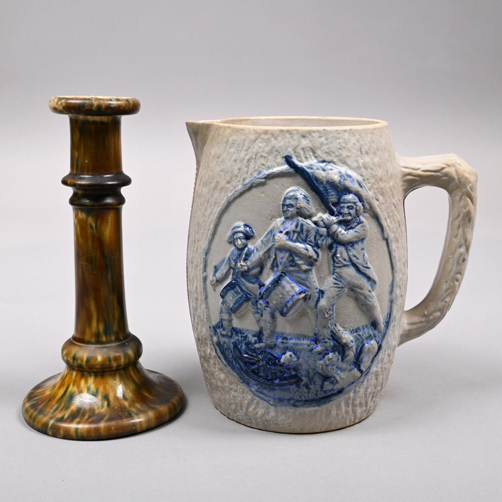 New York Stoneware Beer Jug&Bennington Candlestick: White's Pottery Saltglaze Stoneware Cobalt Blue-Decorated 'Spirit of '76' Beer Jug, Utica, New York, Late Nineteenth Century; and a Bennington Flint Enamel Candlestick, Bennington, Vermont, 1849-58. T