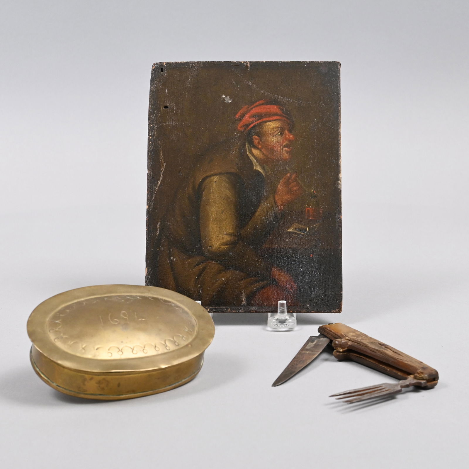 "The Smoker." O/B, Dutch Brass Snuff Box & Utensil: The portrait Dutch school, oil on board, depicting a man wearing a red cap and smoking a long stem pipe; the oval snuff box engraved with the date "1694;" the utensil set a folding steel fork and knif