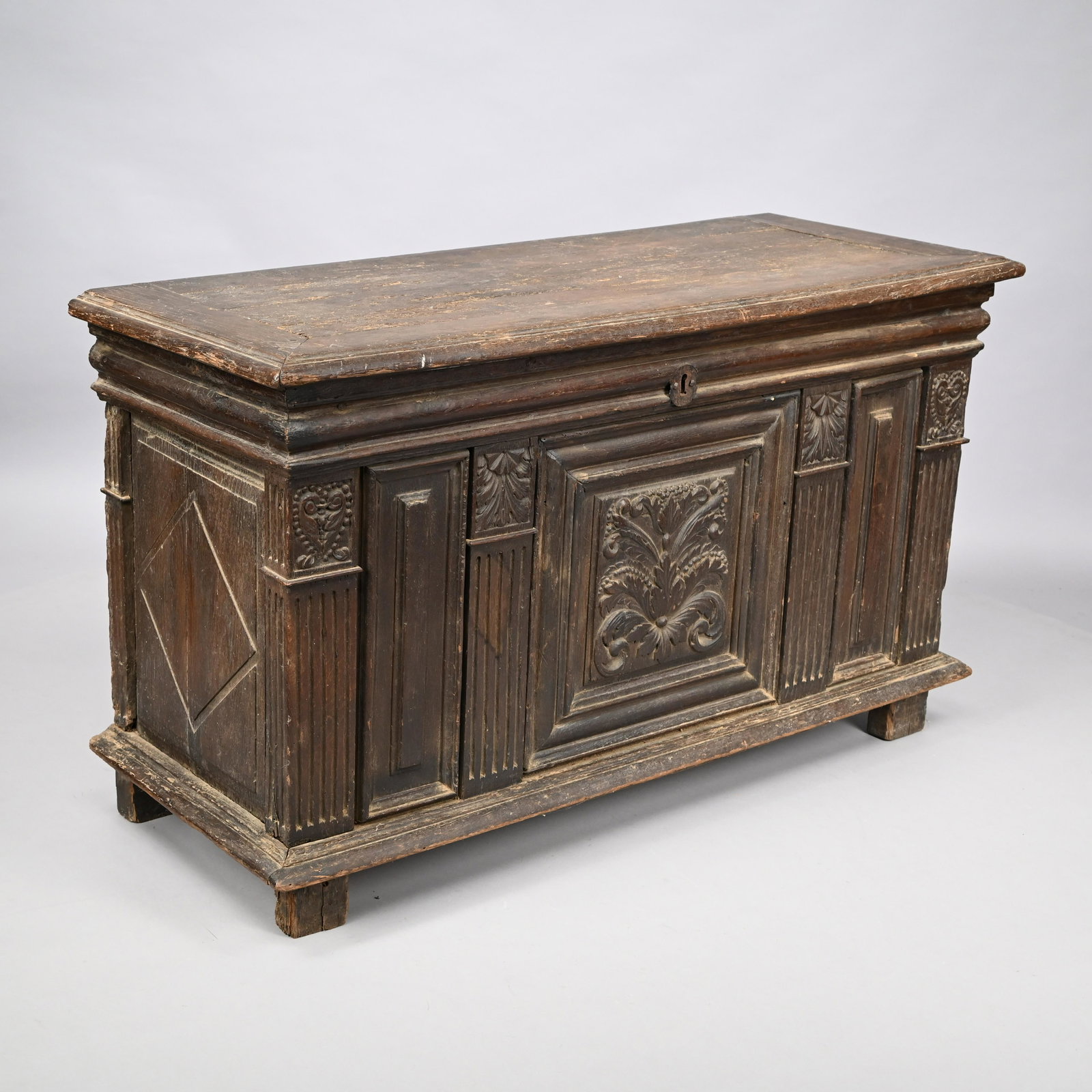French Carved Oak Coffer, Eighteenth Century: The rectangular molded hinged lid above the case, centered by a large panel carved in relief with a stylized flower formed of beaded graduated leaves, flanked by smaller shell and acanthus and beaded