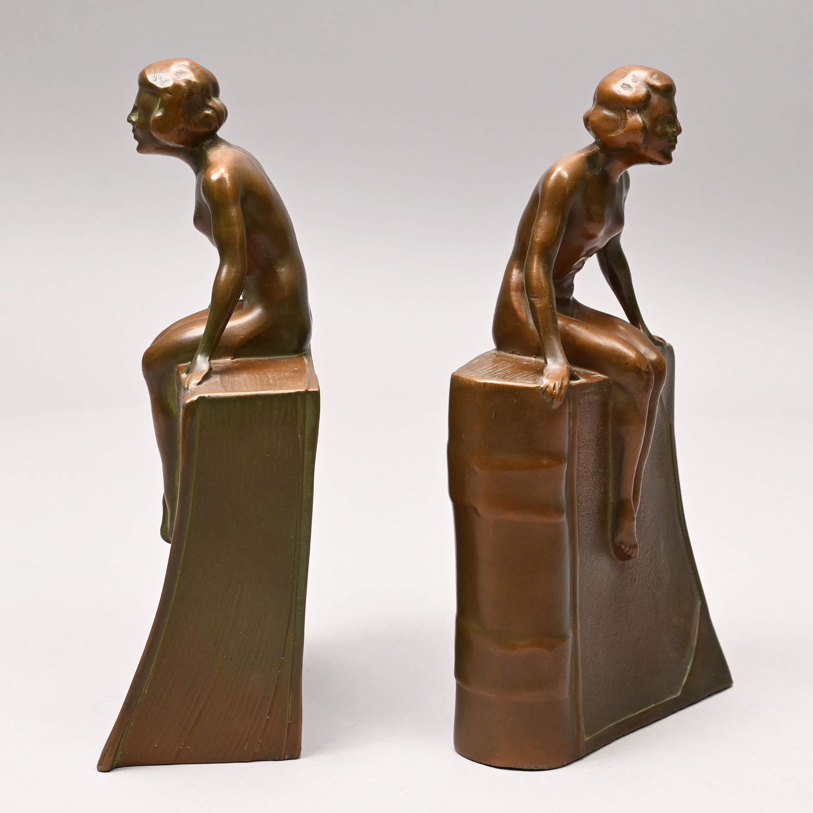Pair of Art Deco Figural Bookends, Littco, 1920-32: Pair of Art Deco Patinated Cast-Iron Figural Bookends, The Littlestown Hardware and Foundry Company, Inc., 1920-32. In copper-colored patination, each cast as a nude woman seated atop a book. H: 8.375