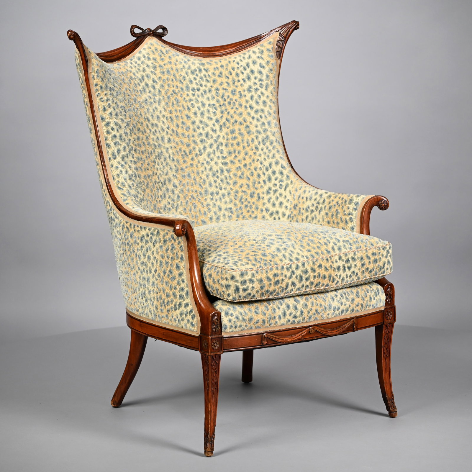 French Belle Epoque Carved Walnut Bergere: French Belle Epoque Carved Walnut Bergere, Late Nineteenth Century. The carved bow-tied crest above the crest rail of drapery folds ending in swag ears, above a padded "batwing" back, the tight seat a