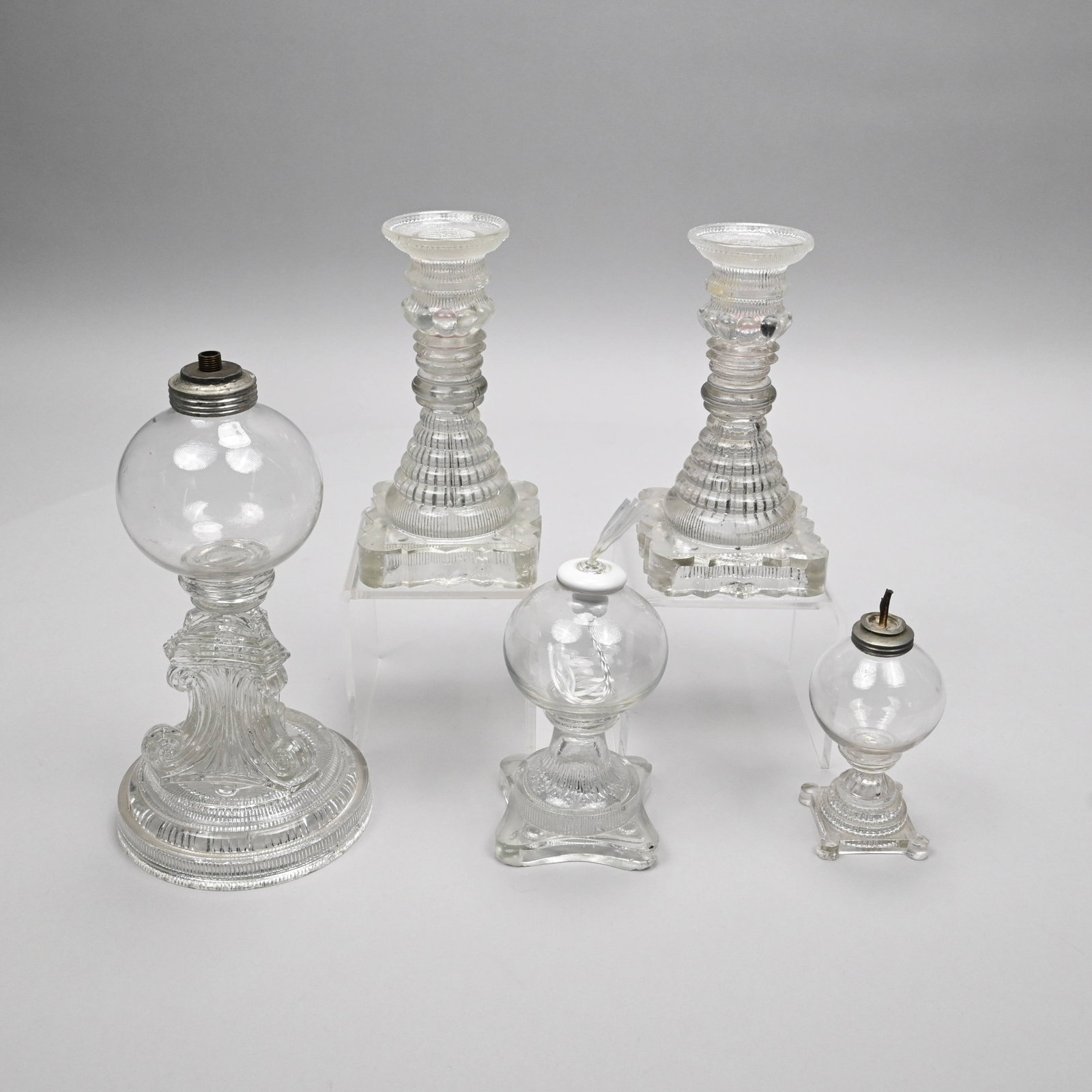 Five New England & Midwest Glass Lighting Devices: Group of New England and Midwest Free-Blown and Pressed Colorless Glass Lighting Devices, 1830-45. Comprising a sparking lamp, the blown font joined by a wafer to the circular stepped inside-ribbed an