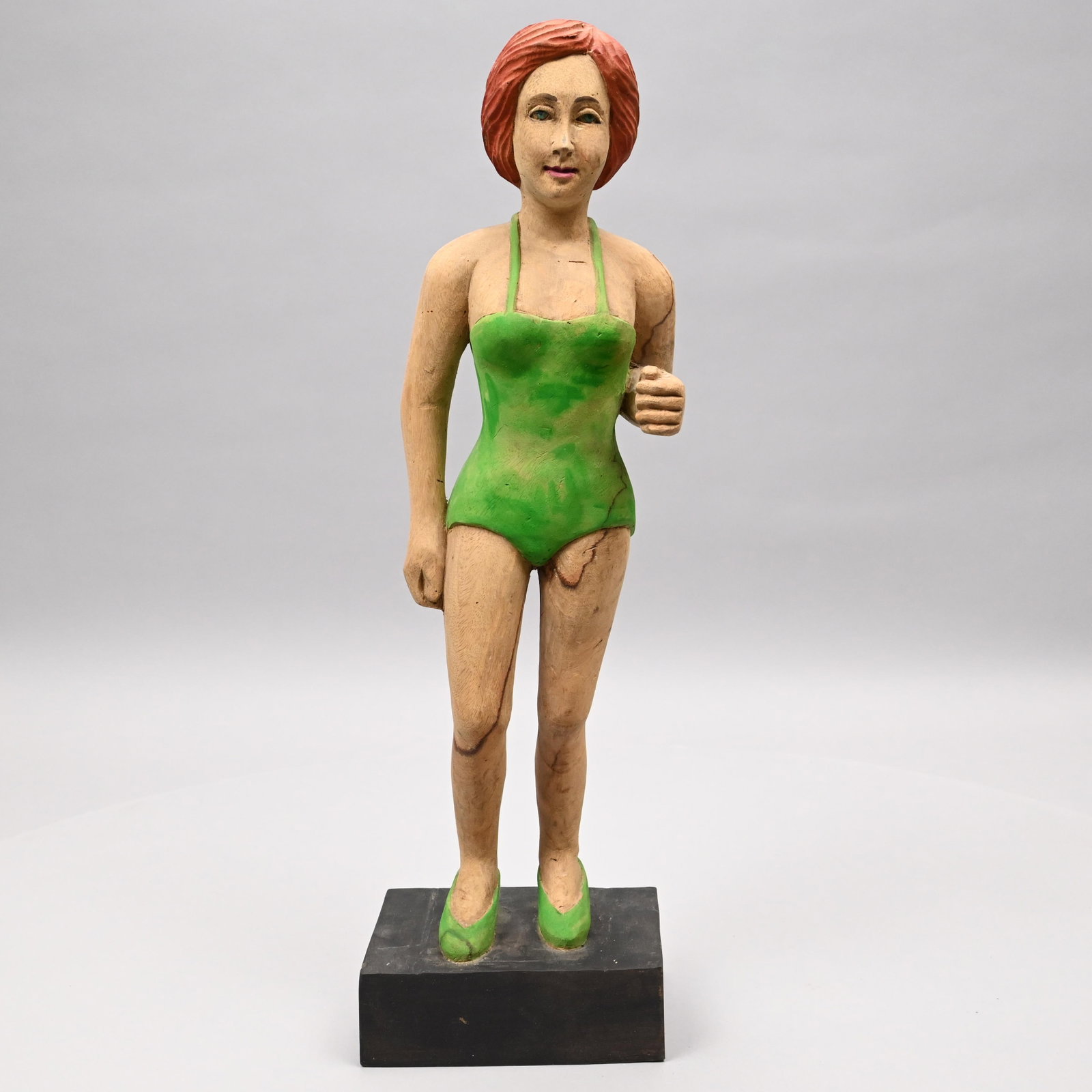 Folk Art Carved Painted Figure of a Bathing Beauty: Folk Art Carved and Painted Figure of a Bathing Beauty. Wearing a green 1950's style one-piece suit and green high heels, mounted on a plinth base. H: 20 in. (Overall), W: 6.25 in., D: 4.25 in.