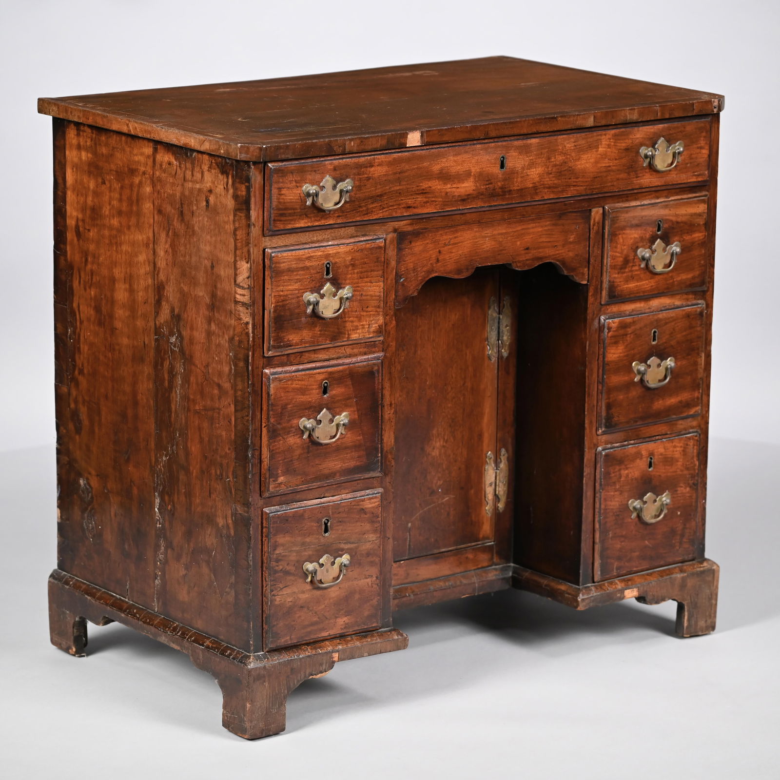 George III Mahogany Diminutive Kneehole Desk: George III Mahogany Diminutive Kneehole Desk. The rectangular top within an applied edge and canted corners, above a drawer over a cupboard door opening to a shelf and flanked by two banks of three mo