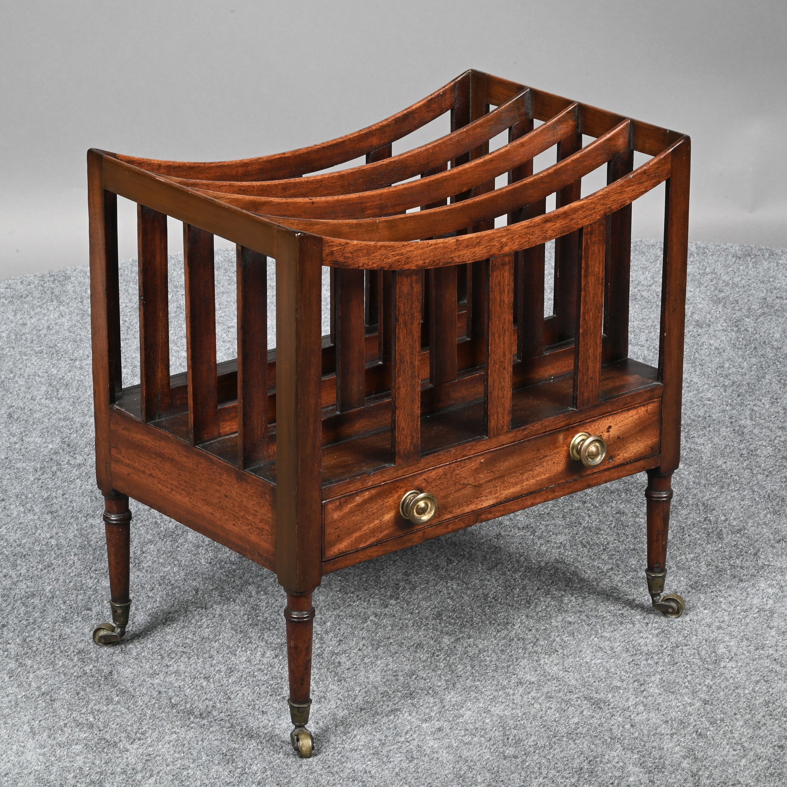 George III Mahogany Canterbury: George III Mahogany Canterbury, Early Nineteenth Century. Divided into four curved sections above a drawer, raised on ring-turned tapered legs, on casters. H: 19 in., W: 18 in., D: 12 in.