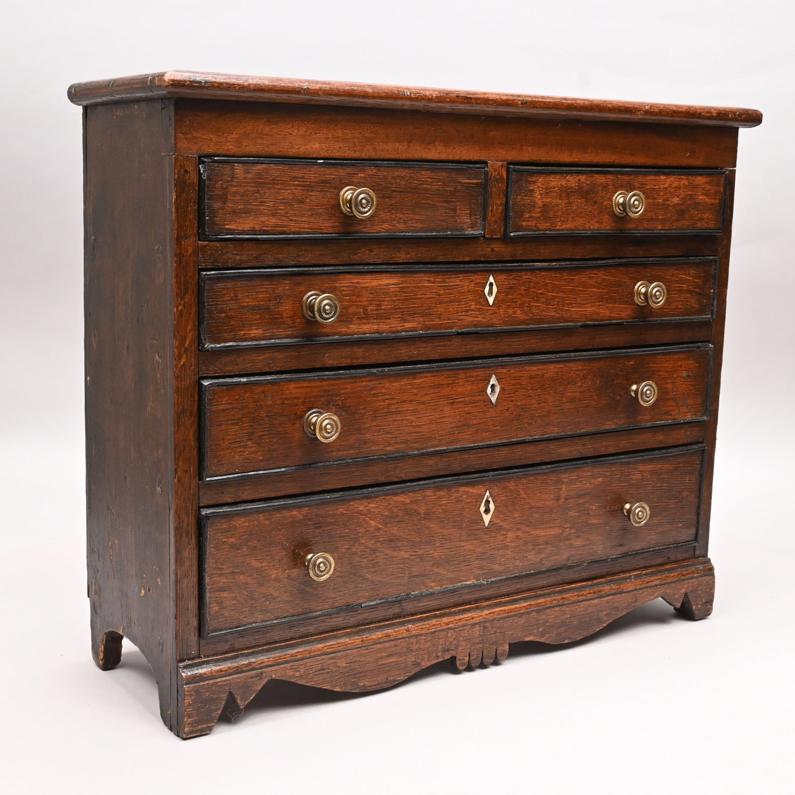 George III Oak Children's Chest of Drawers: George III Oak Children's Chest of Drawers, Nineteenth Century. The rectangular top with applied edges above two aligned cockbeaded drawers over three graduated drawers, each inlaid with a bone escutc