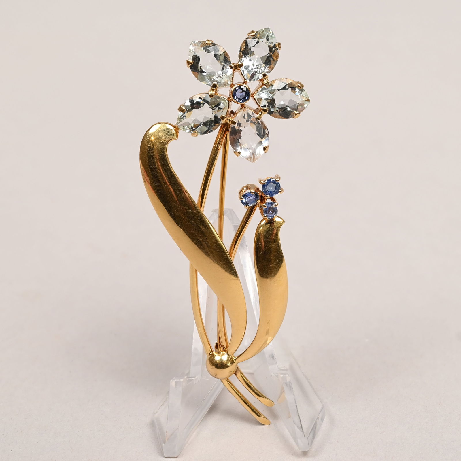 Cartier 14k Gold, Aquamarine & Sapphire Brooch: Cartier 14k Yellow Gold, Aquamarine and Sapphire Flower Brooch. The stems affixed with curled leaves, the flower set with aquamarine petals centering a sapphire and the stem below with three sapphire