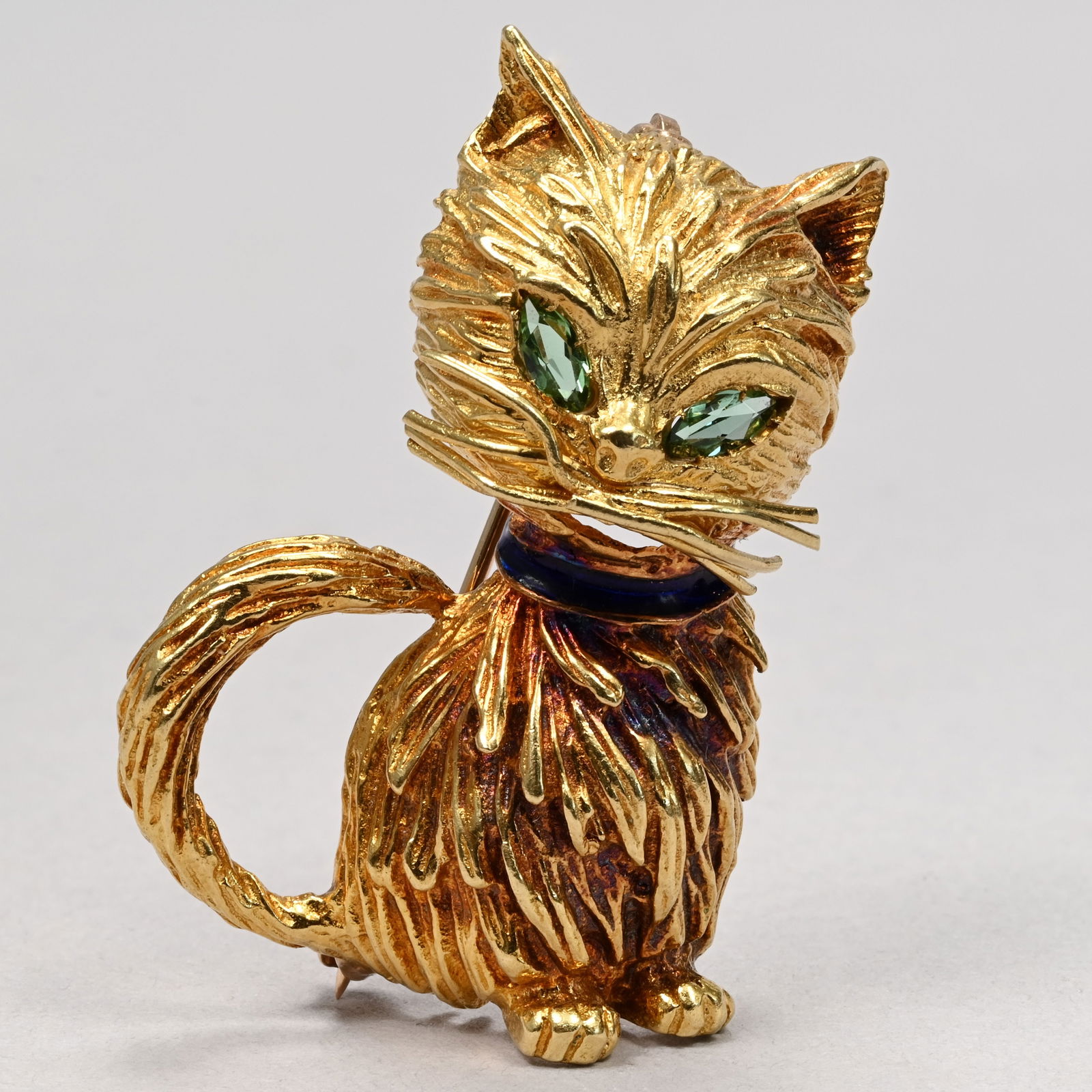 18k Yellow Gold and Emerald Seated Cat: Mid-Century Modern 18k Yellow Gold and Emerald Seated Cat. Set with faceted emerald eyes and wearing a purple enamel collar, unmarked but the cat tested 18k and the clasp 14k.12.3gH: 1.4 in., W: 1 in.