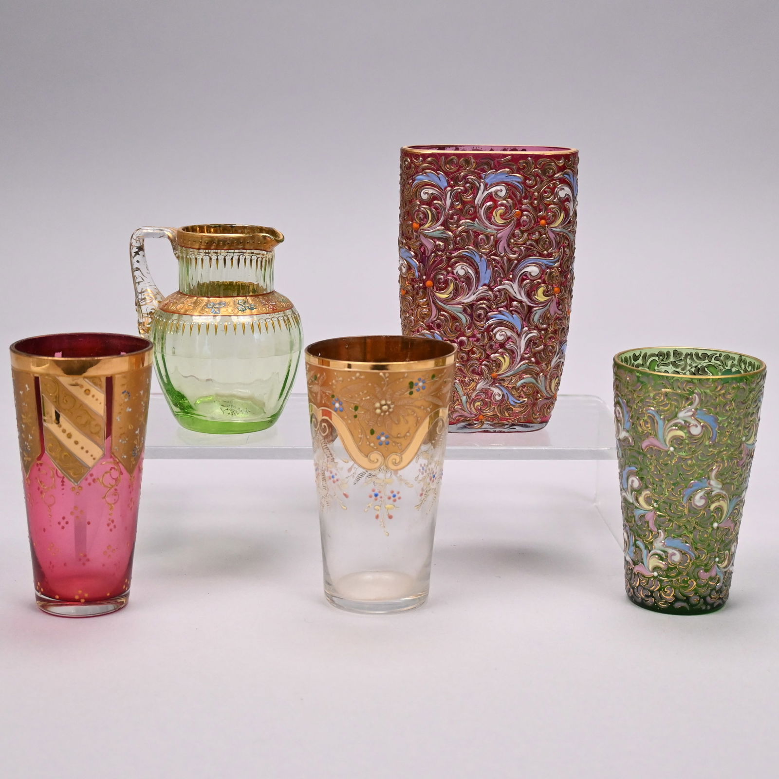 Five Bohemian Enamelled and Gilt Glass Articles: Five Bohemian and Austrian Cut, Enamelled and Gilt Glass Articles, Late 19th-Early 20th Century. Comprising a miniature pitcher, Ludwig Moser & Sons, 1890-1925, in shaded pale to darker green glass