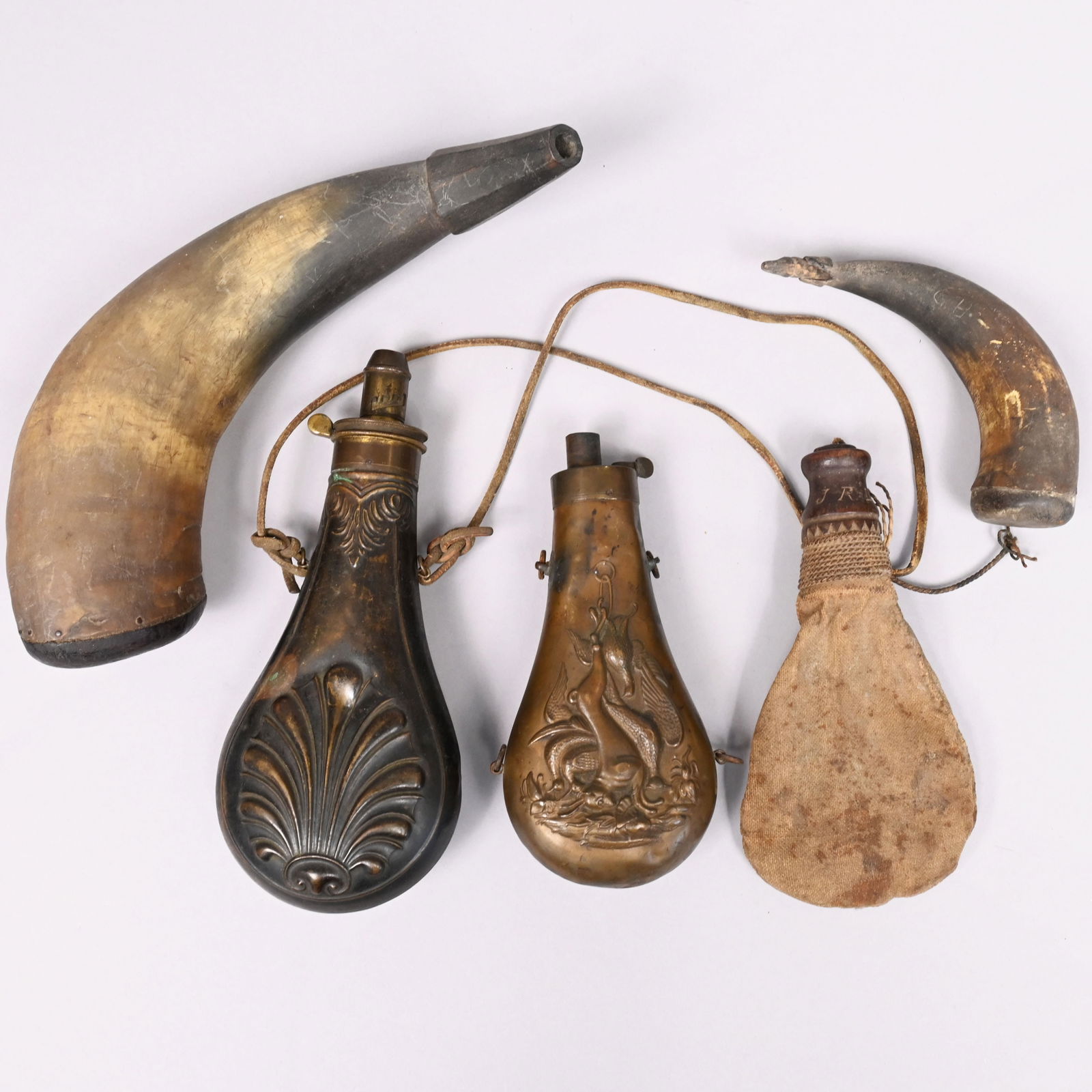 Five Powder Horns/ Flasks: Comprising a Civil War era embossed copper and brass 'Dead Game' powder flask, attributed to James Dixon & Sons, Sheffield; a Civil War 'Shell and Bush' copper and brass powder flask, American Flask